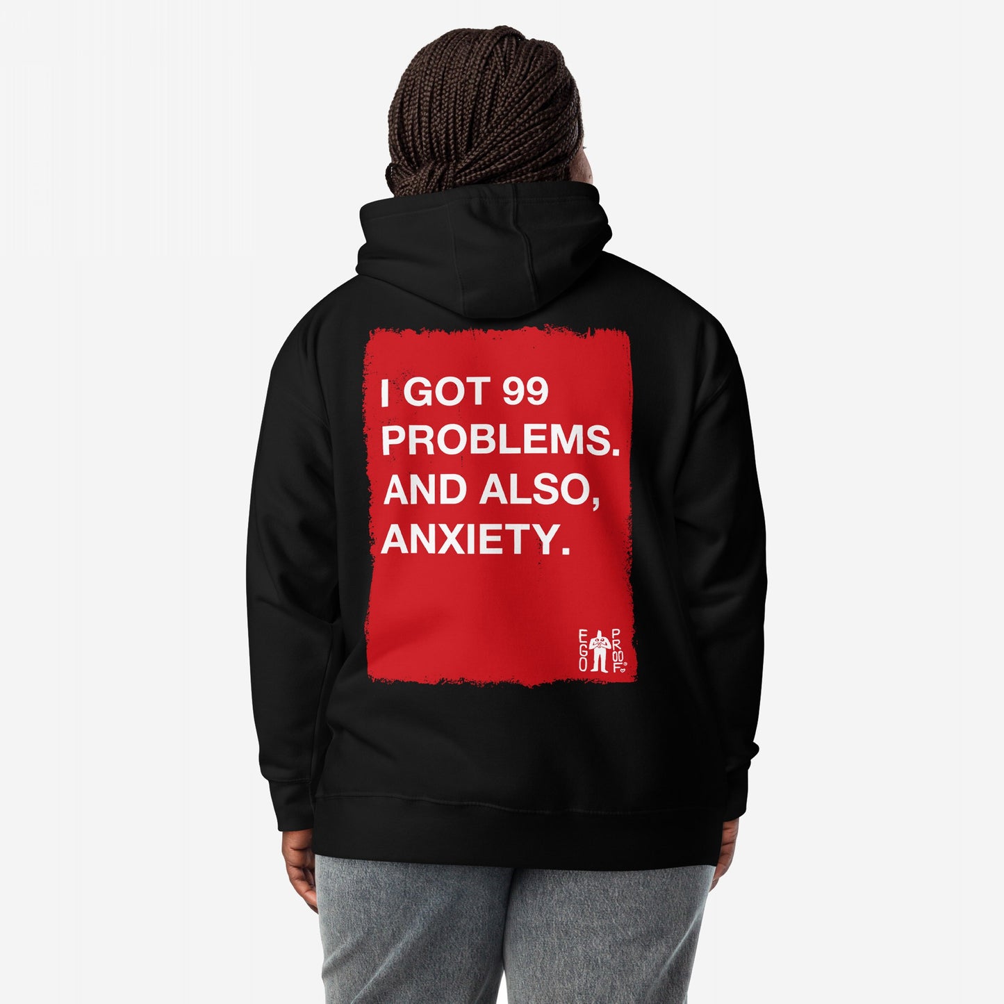 99 Problems Hoodie EU features a bold red square with white text about stress and anxiety on the back, worn by a person with braided hair in gray pants.