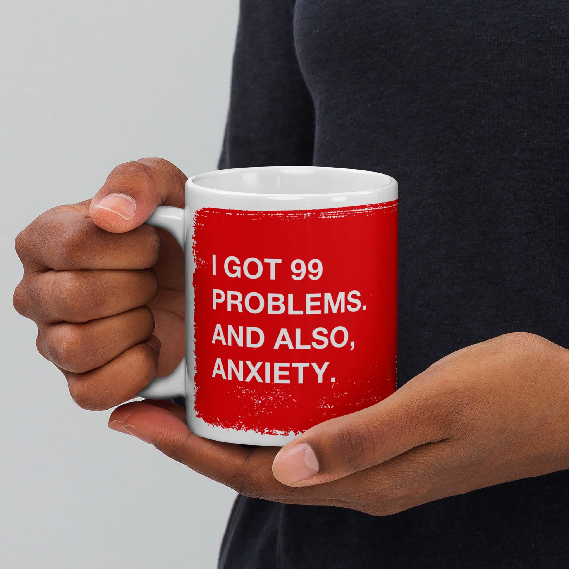 Person holding a white ceramic mug with red print saying "I got 99 problems. And also, anxiety." 99 Problems Mug.