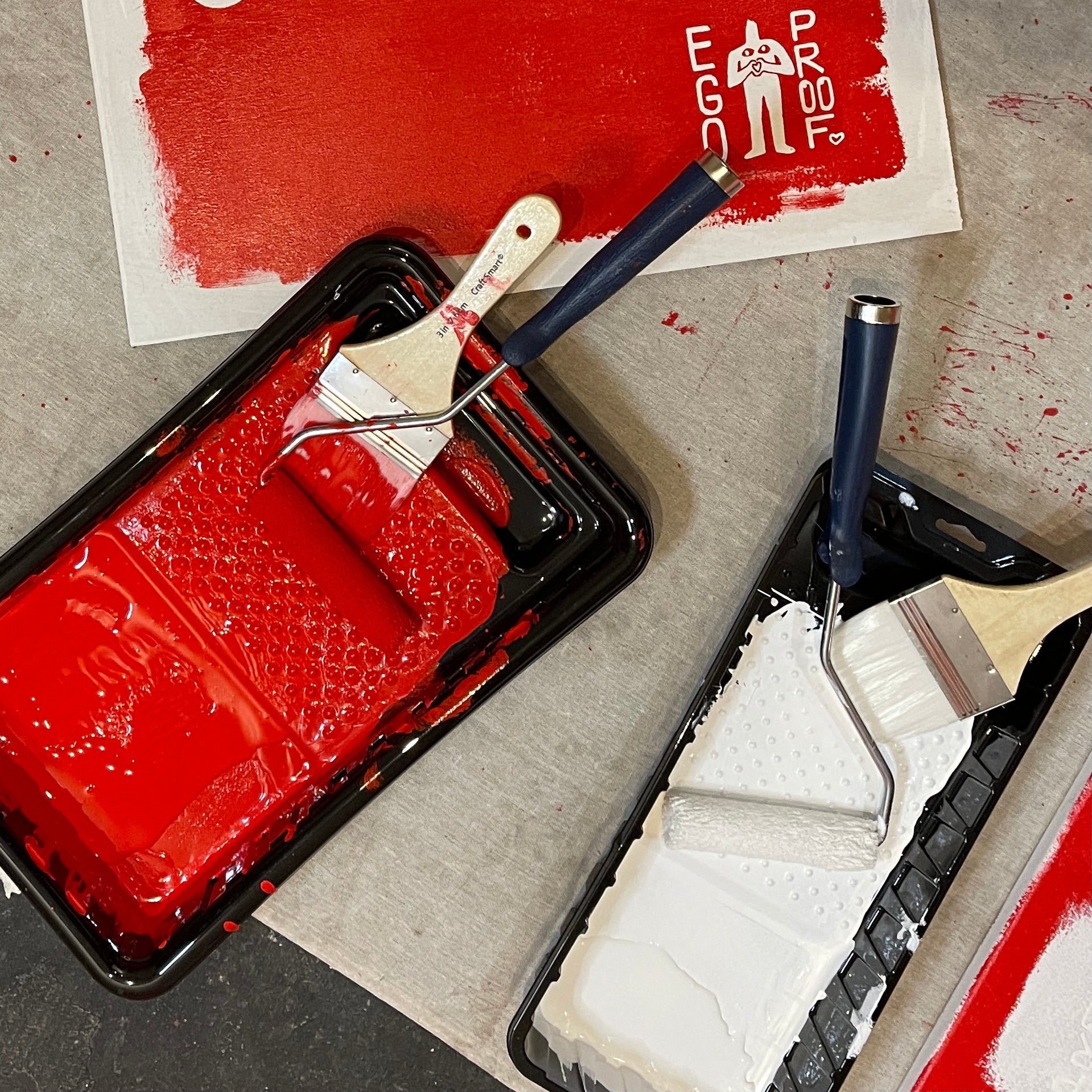 EGOPROOF paint tray with red paint, roller, and brush on a gray surface with a visible brand logo.