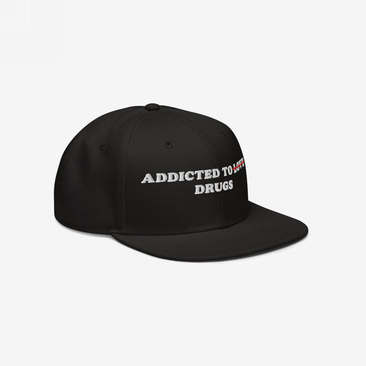 The Egoproof Addicted To Love / Drugs Hat is a black embroidered snapback featuring ADDICTED TO LOVE with LOVE in red crossed out and replaced by DRUGS in white, shown on a plain white background.