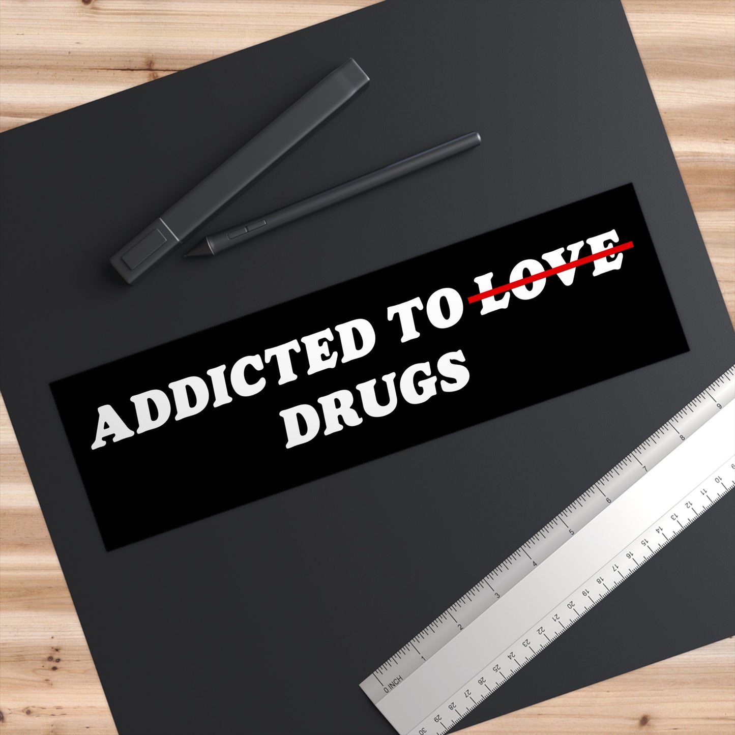 Addicted To Love / Drugs Sticker & Magnet on a black drawing mat with a stylus, sleeve, and ruler. The text humorously reflects mental health themes, capturing Egoproof's bold statement style.