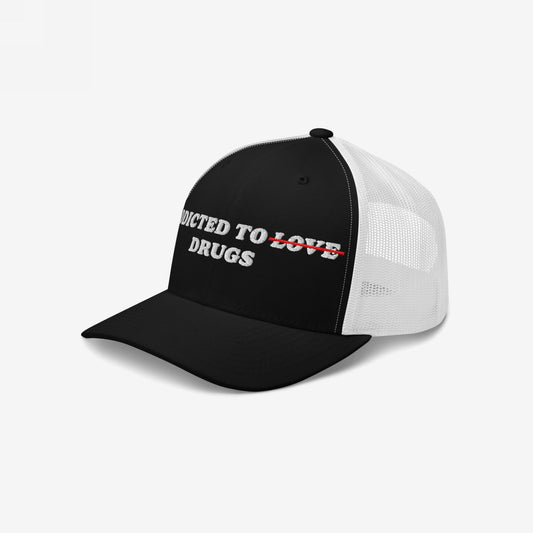 The Egoproof Addicted To Love / Drugs Hat features a black and white design with ADDICTED TO ~~LOVE~~ DRUGS on the front—LOVE is crossed out in red and replaced by DRUGS for a bold mental health statement.