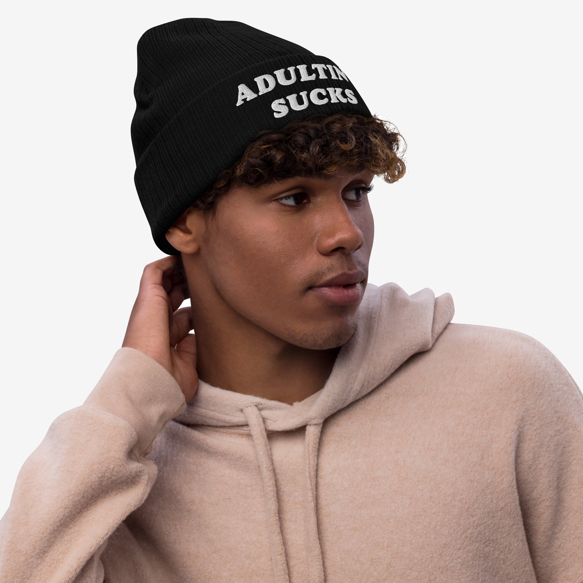 Young man wearing an Adulting Sucks knit beanie, conveying a relatable message. The hat is perfect for those overwhelmed by everyday demands, aligning with Egoproof's mission to express mental health struggles.