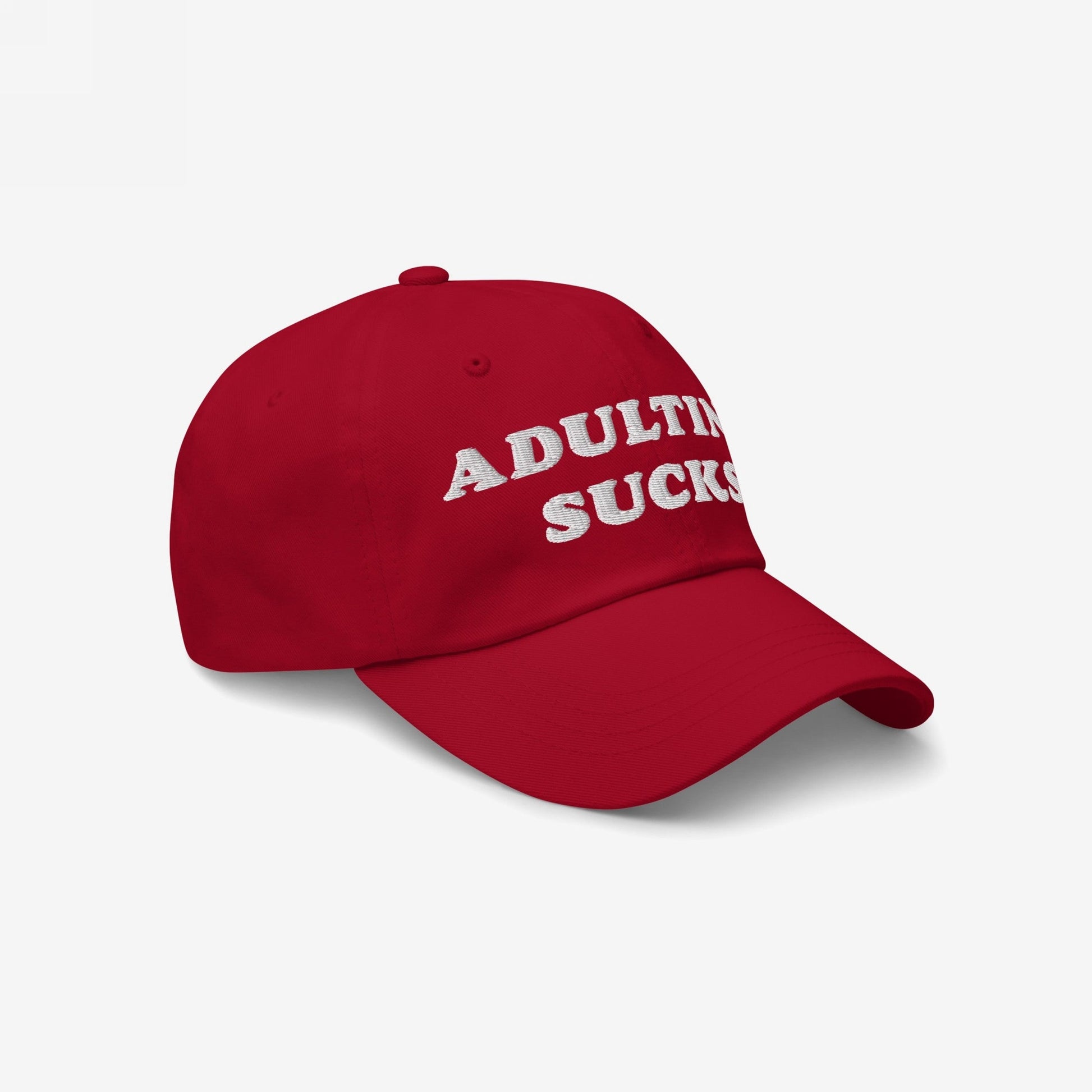 Red baseball-style cap with white embroidered lettering reading “ADULTING SUCKS,” the Adulting Sucks Hat. Ideal for expressing mental health struggles with style and honesty, supporting NAMI.