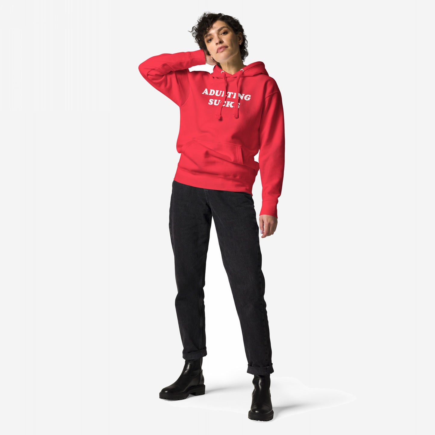 Person in a bright red Adulting Sucks Hoodie EU, paired with slim-fit dark jeans and chunky black ankle boots, poses casually. This midweight, unisex hoodie embodies comfort and a playful, sarcastic statement.
