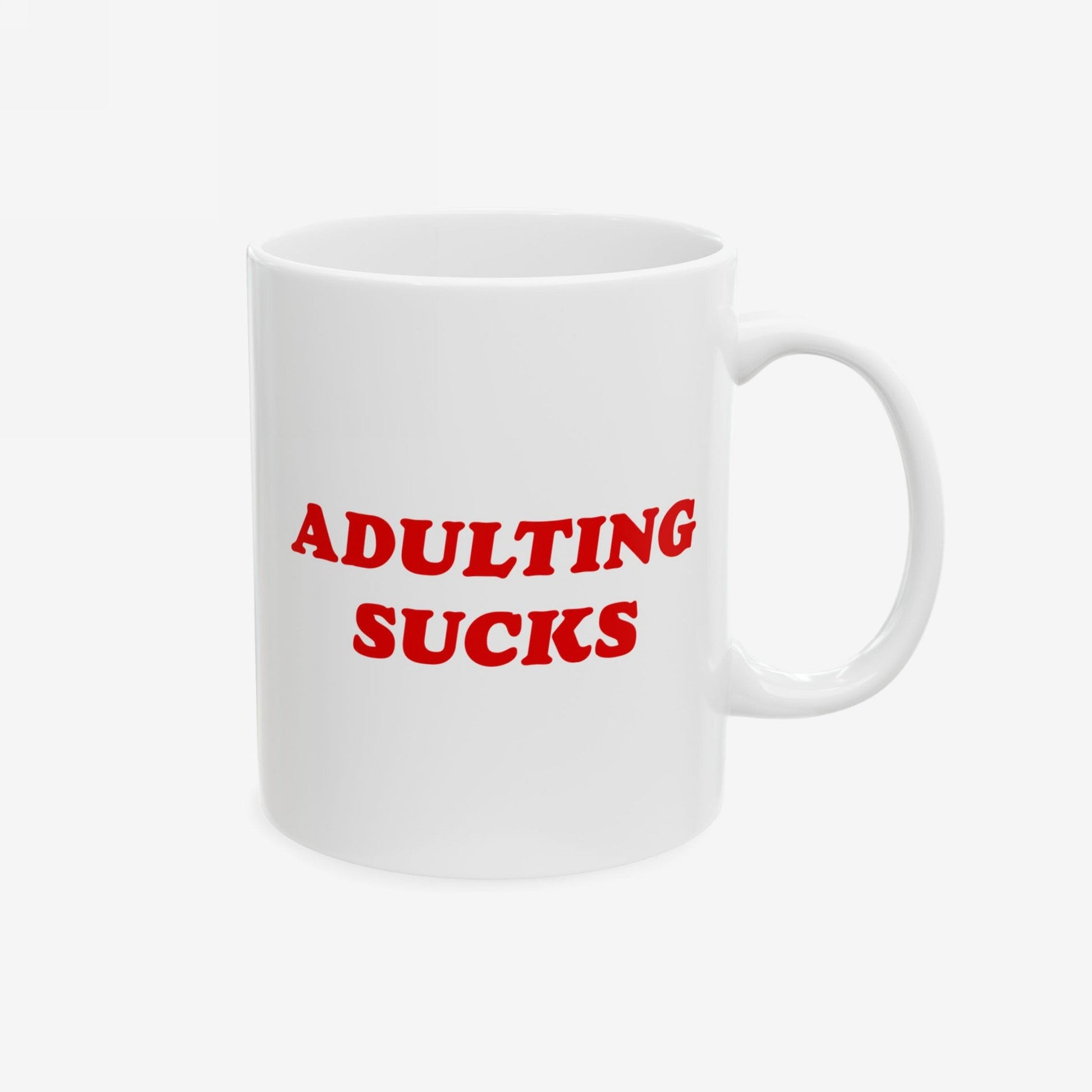 Plain white ceramic mug with bold red text reading “ADULTING SUCKS.” Perfect for office rebels, this 11 oz. or 15 oz. Adulting Sucks Mug offers humor with a standard handle. Dishwasher-safe.