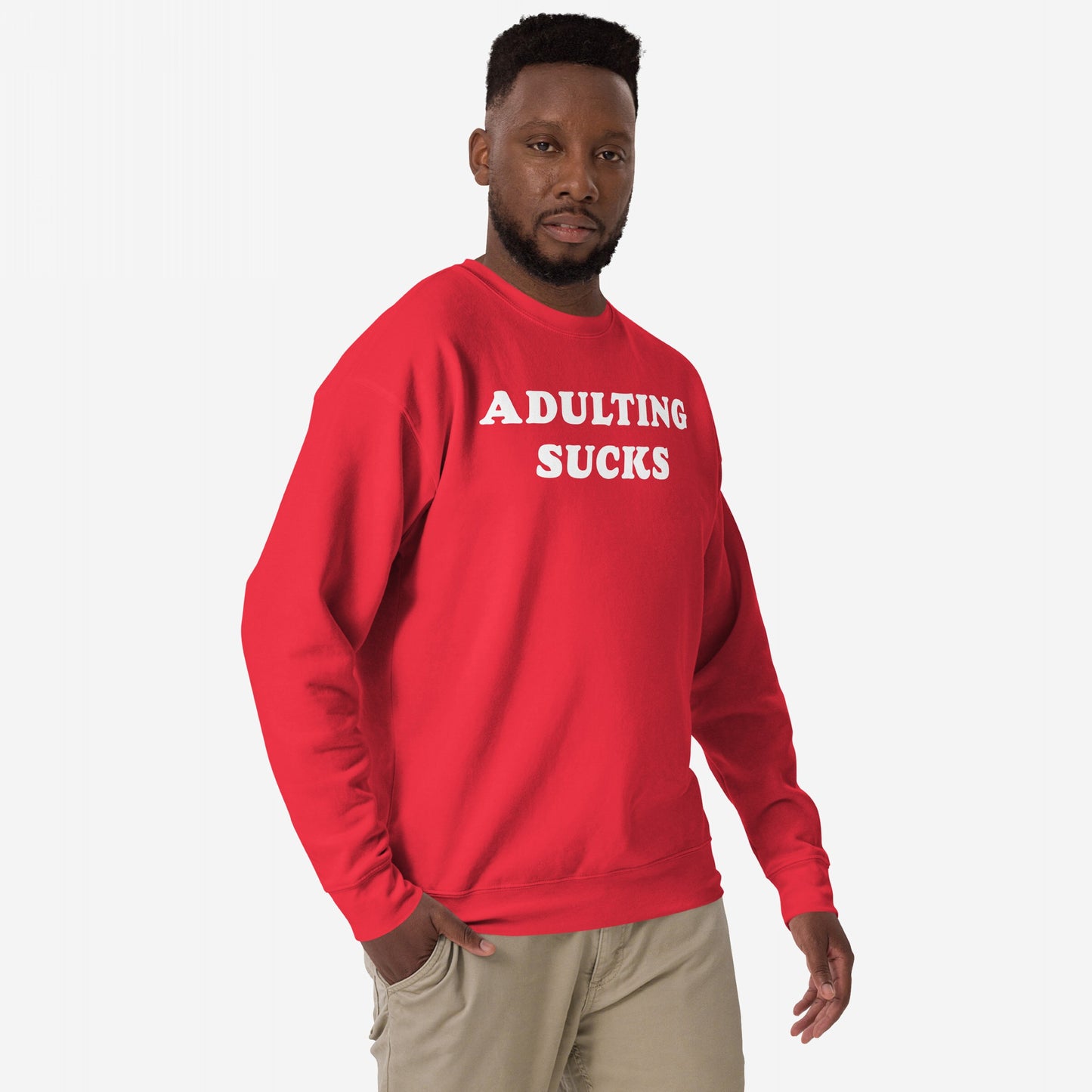Man in Adulting Sucks Sweatshirt EU, wearing light-tan pants, stands against a plain background. The red crewneck features bold white lettering, perfect for expressing burnout with style and humor.