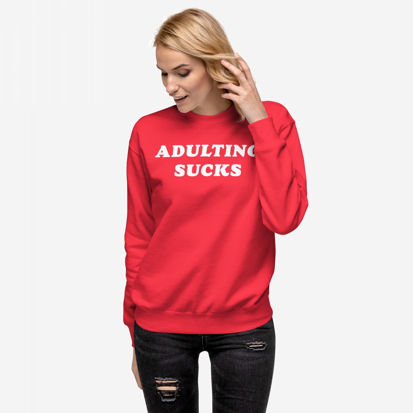 Young woman models the Adulting Sucks Sweatshirt EU, a bright red crewneck with bold white lettering, paired with black distressed skinny jeans, embodying Egoproof's powerful statement apparel for life's challenges.