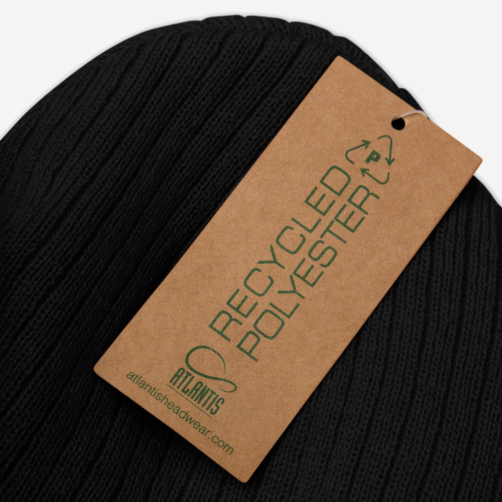 Anti-Fascist Beanie close-up, featuring a cardboard hang-tag with a recycling symbol and RECYCLED POLYESTER text. Brand: ATLANTIS. A bold statement piece for resistance and mental health advocacy.