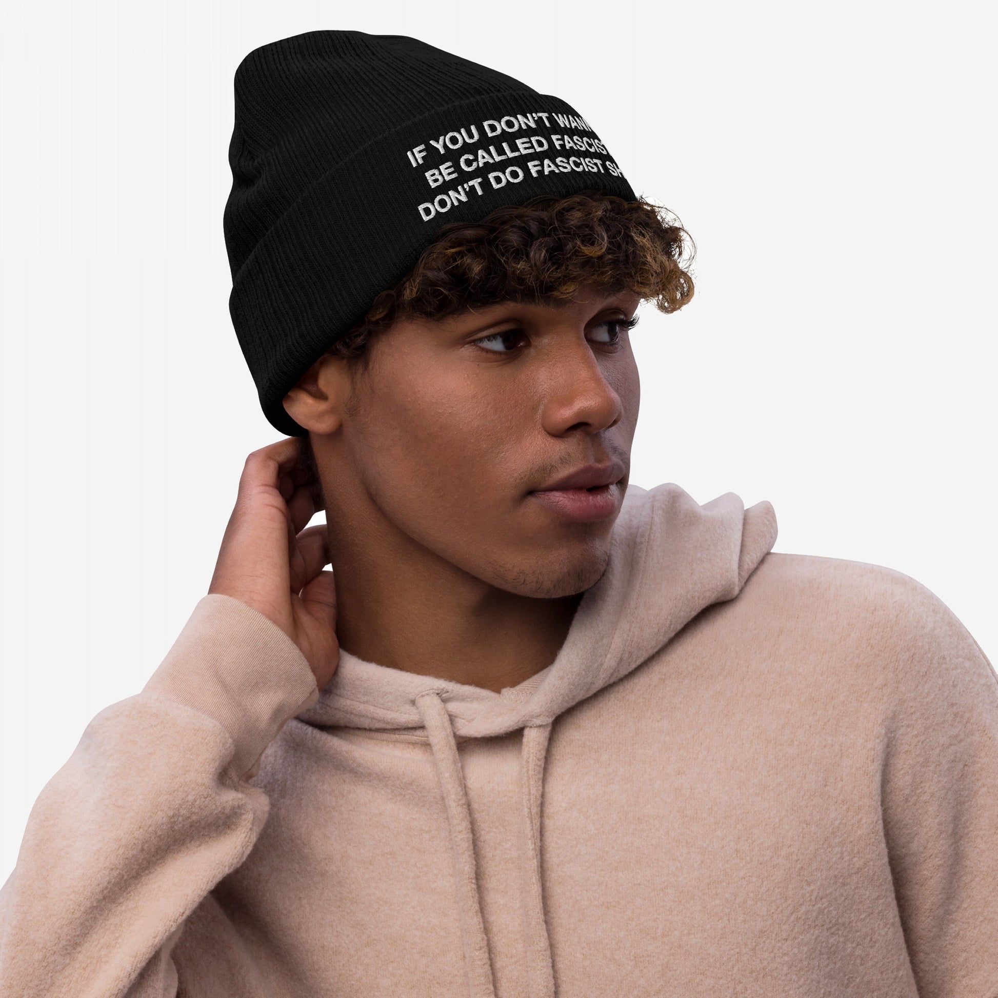 Anti-Fascist Beanie: A young person models this bold, light-beige hoodie and black knit beanie, emblazoned with a defiant anti-fascist message, ideal for expressing resistance and standing against hate.