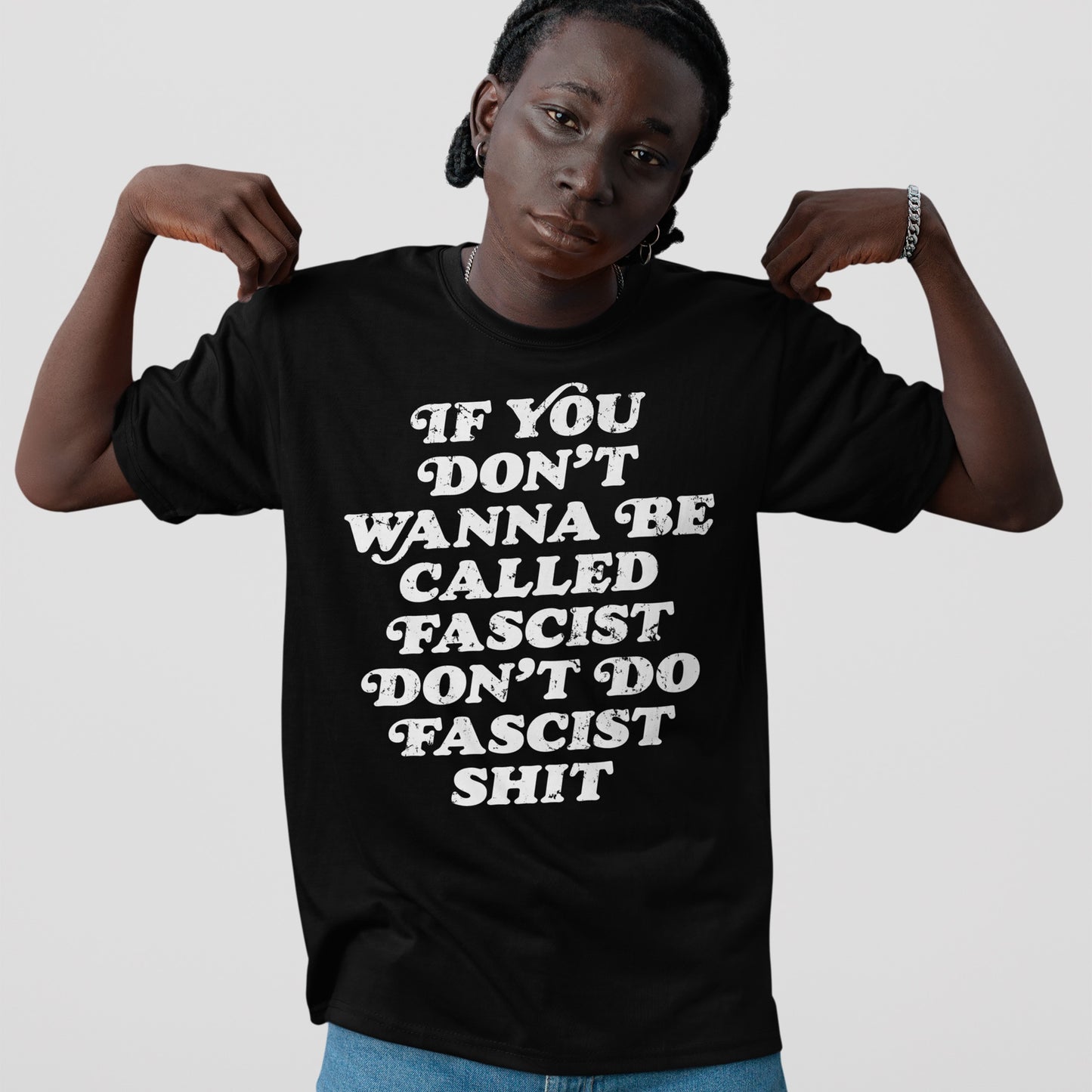 Anti-Fascist T-shirt with bold white slogan, “IF YOU DON’T WANNA BE CALLED FASCIST DON’T DO FASCIST SHIT,” worn by person pointing at it, embodying defiance and accountability.