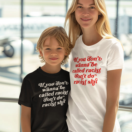 Anti-Racist Kids T-shirt: A young boy wears a black T-shirt with a bold anti-racist message, standing confidently beside a woman in an airport, embodying empowerment and courage for the next generation.