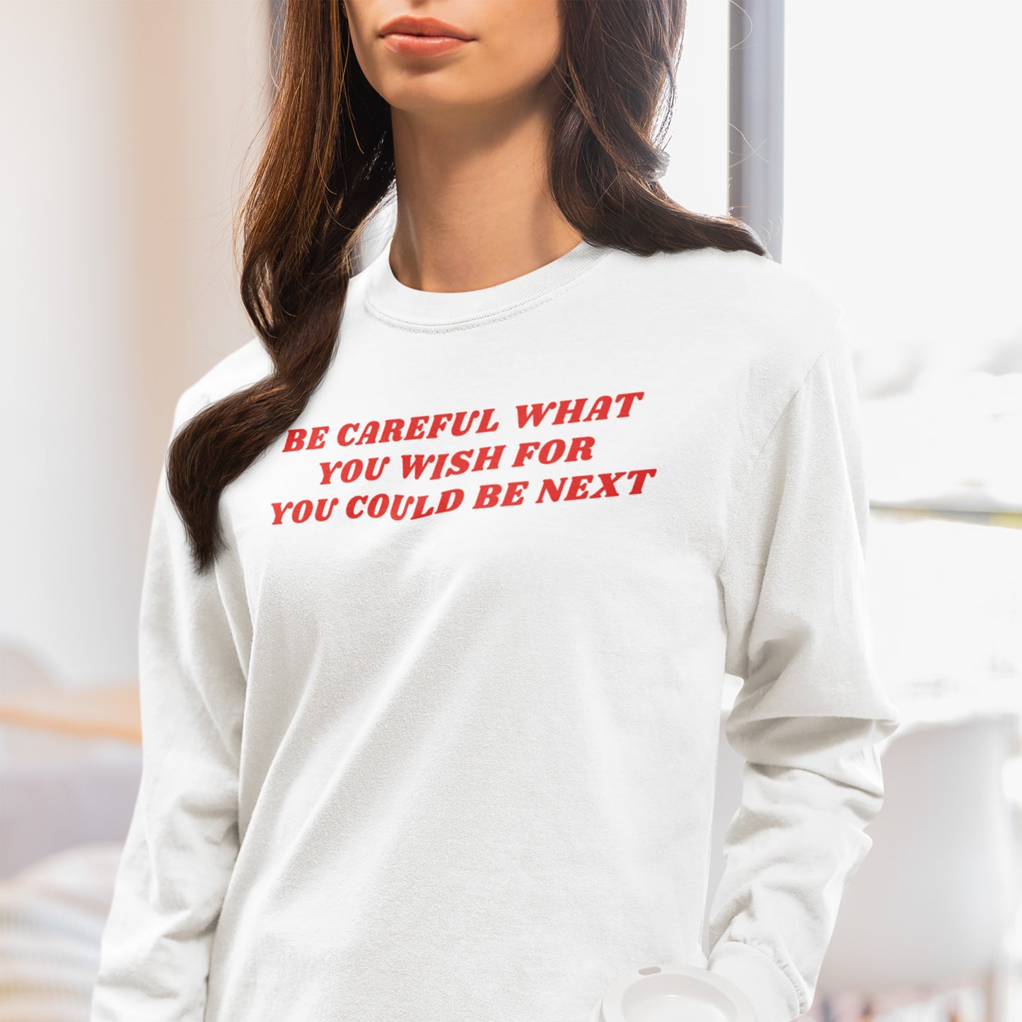 Woman wearing a white Be Careful Long Sleeve T-shirt with red bold text reading "Be Careful What You Wish For You Could Be Next.