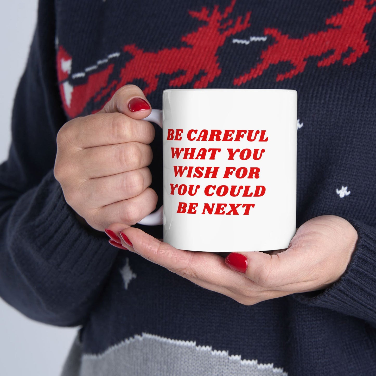 Person holding the Be Careful Mug with bold red text, wearing a dark festive sweater. This ceramic mug embodies vigilance and realism, designed for the politically aware and socially exhausted.
