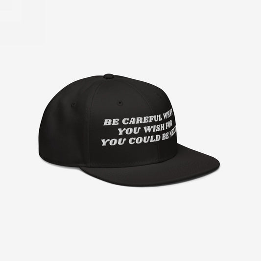 Black snapback cap with flat brim features bold white embroidery: BE CAREFUL WHAT YOU WISH FOR YOU COULD BE NEXT, embodying the Be Careful Hat's unapologetic resistance spirit, ideal for activism and expression.