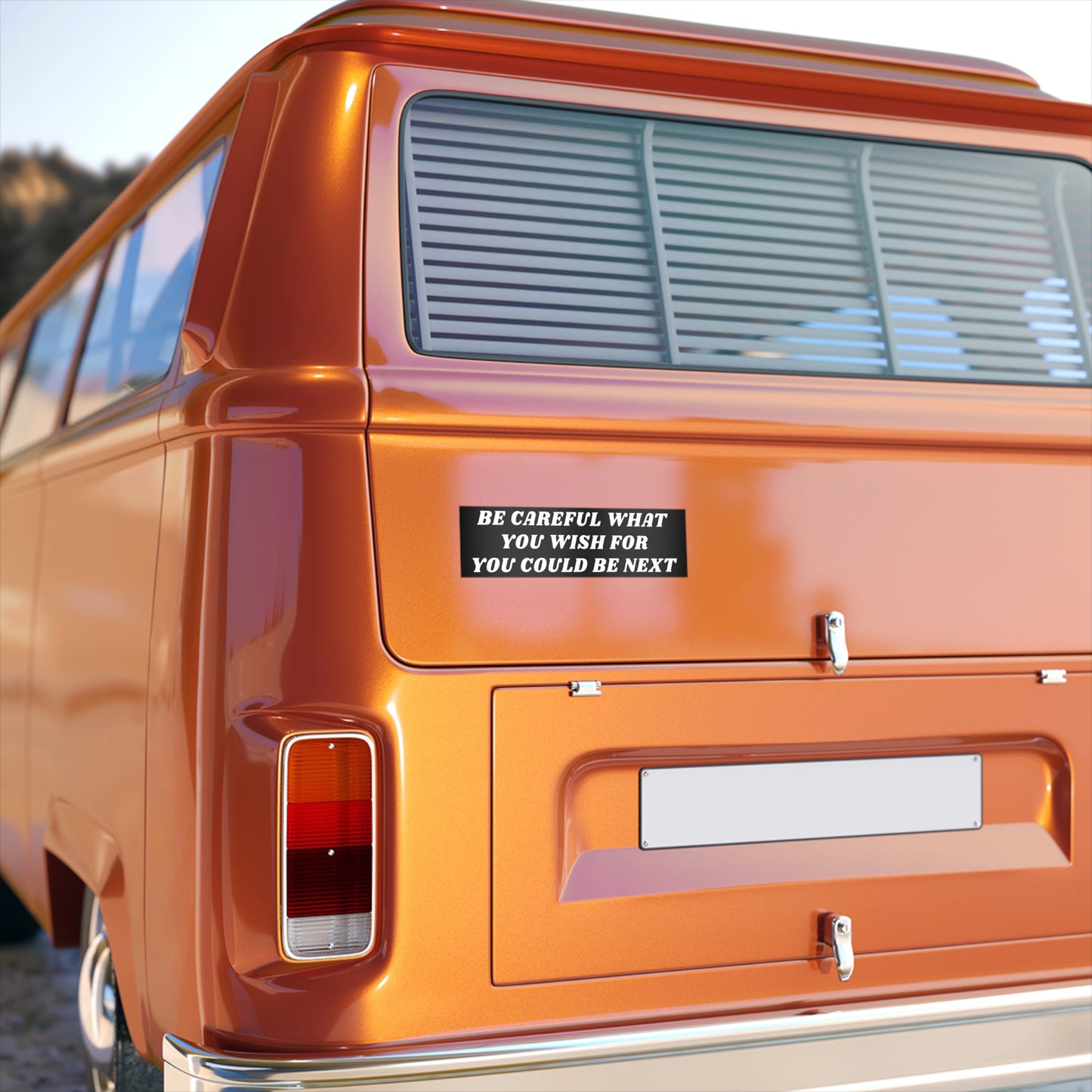 Rear view of an orange vintage-style van displaying the Be Careful Sticker & Magnet with bold white text. The sticker, a silent protest, warns BE CAREFUL WHAT YOU WISH FOR YOU COULD BE NEXT.