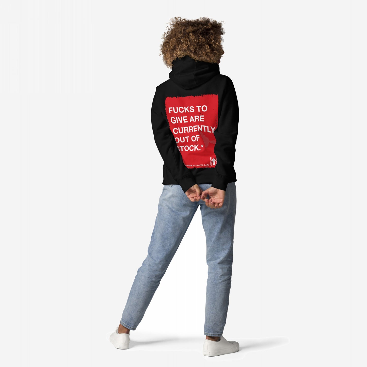 Person in black Fucks To Give Hoodie EU with bold red statement on back, light-wash jeans, and white sneakers, standing relaxed, symbolizing stylish apathy and comfort.