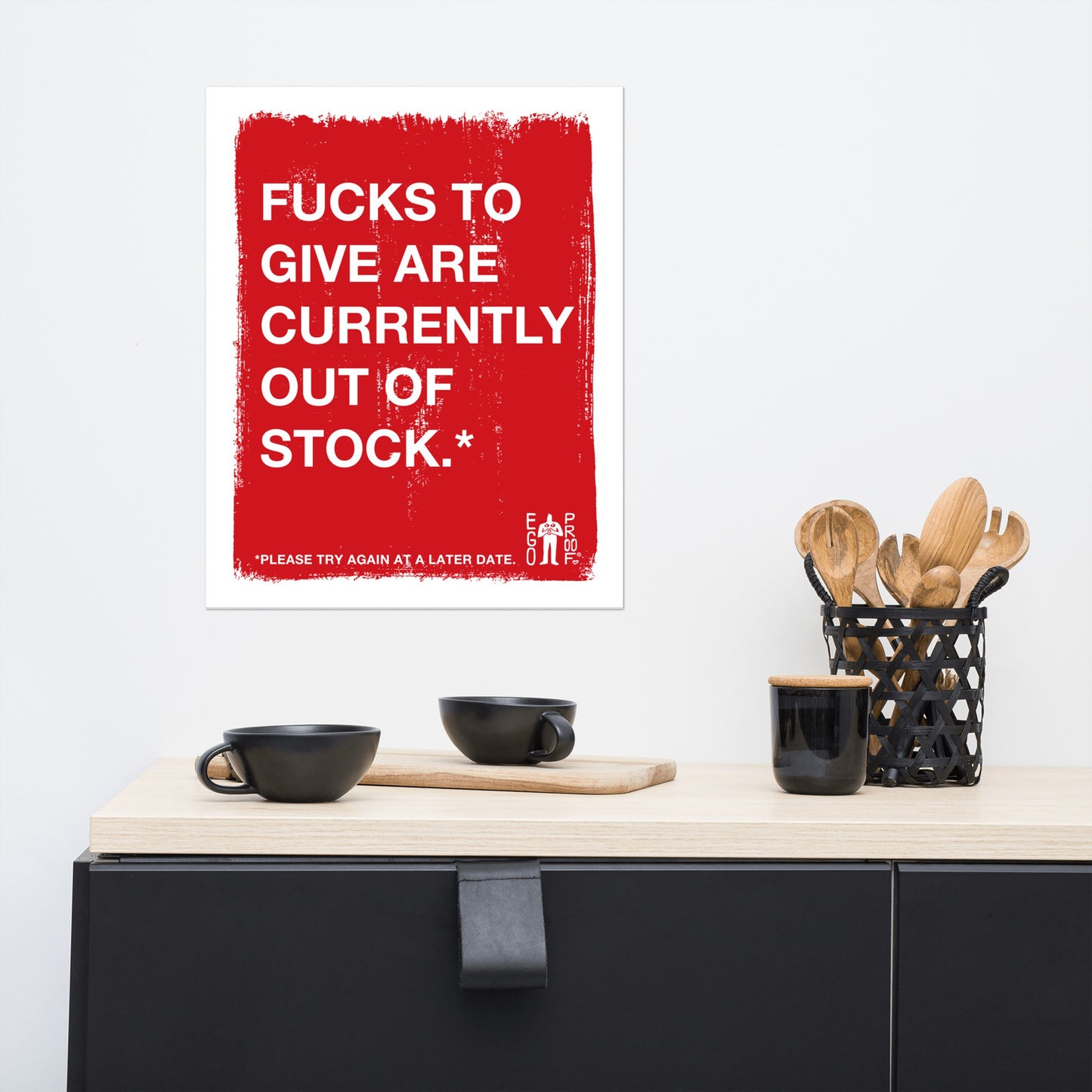 Fucks To Give Giclée Print in a modern kitchen scene, featuring bold white text on a distressed red background, humorously capturing burnout. Displayed above a sleek counter with black mugs and utensils.