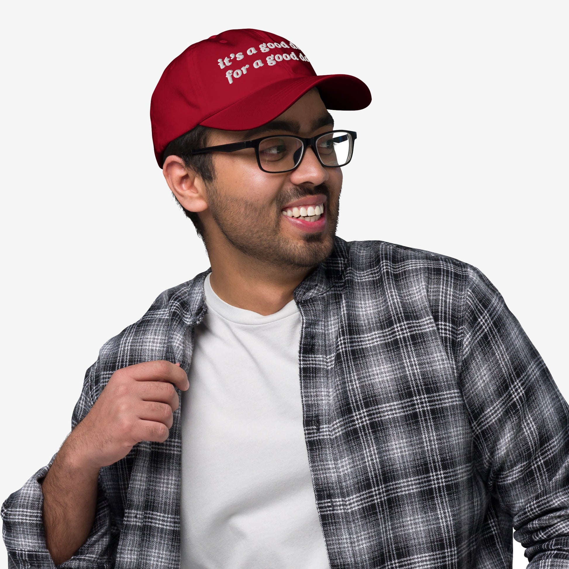 Young man wearing the Good Day Hat, a red baseball cap with it's a good day for a good day embroidered, styled with black-frame glasses and a plaid shirt, embodying positivity and mental health advocacy.