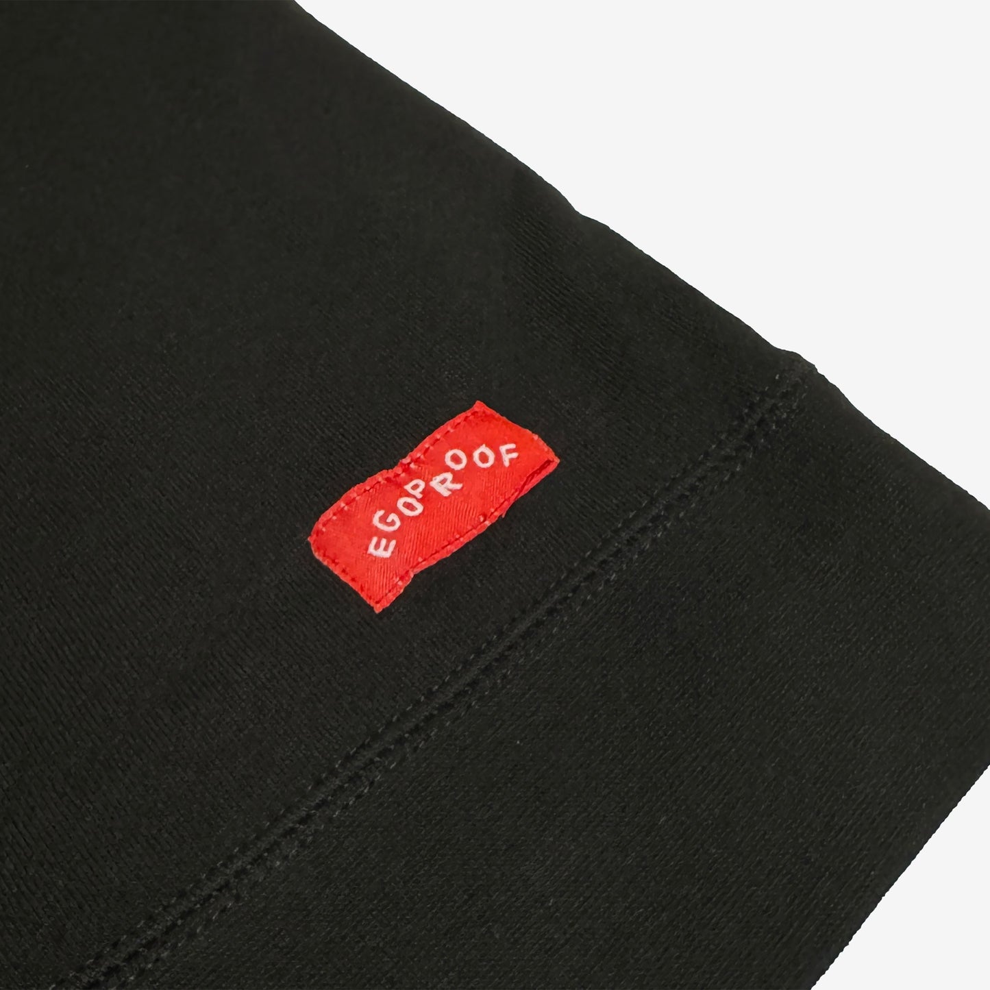 The Good Day Sweatshirt features a close-up of its hem with a small red woven EGOPROOF label, embodying subtle positivity in line with Egoproof’s mental health-focused apparel ethos.