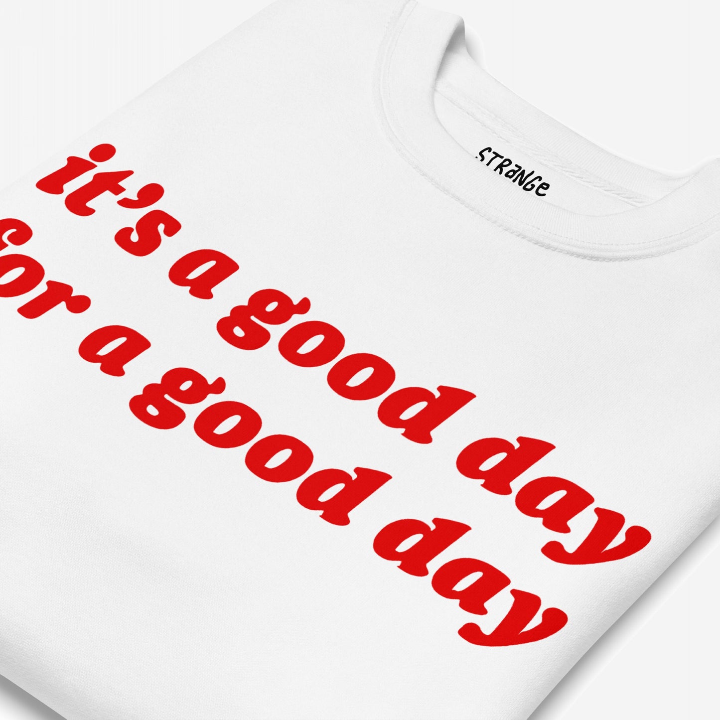 Good Day Sweatshirt EU, folded close-up, features bold red text it’s a good day for a good day on the front, offering a comforting, optimistic message. Partial internal label visible near collar.