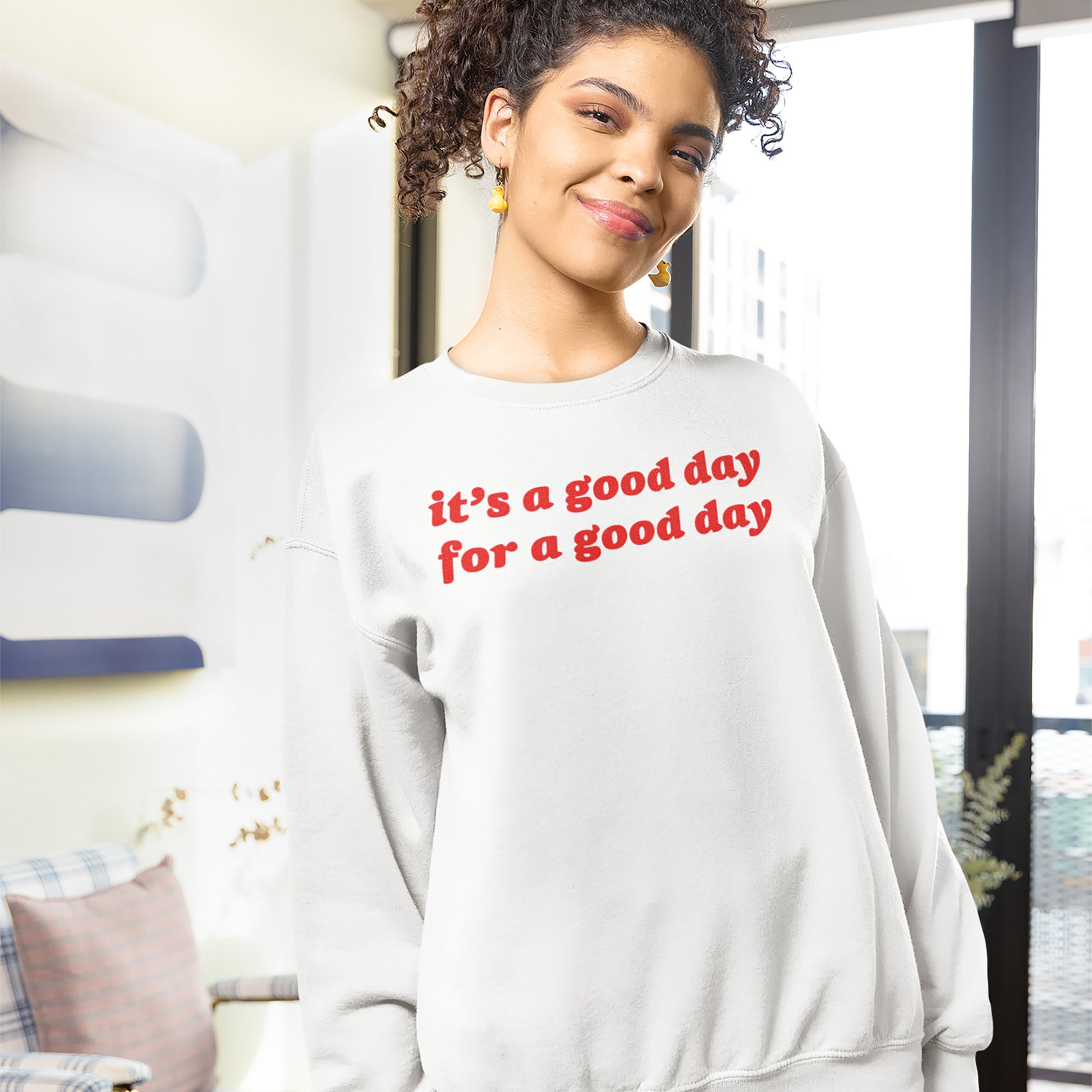 Smiling woman wearing a white Good Day Hoodie & Sweatshirt with red uplifting text in a bright, cozy indoor setting