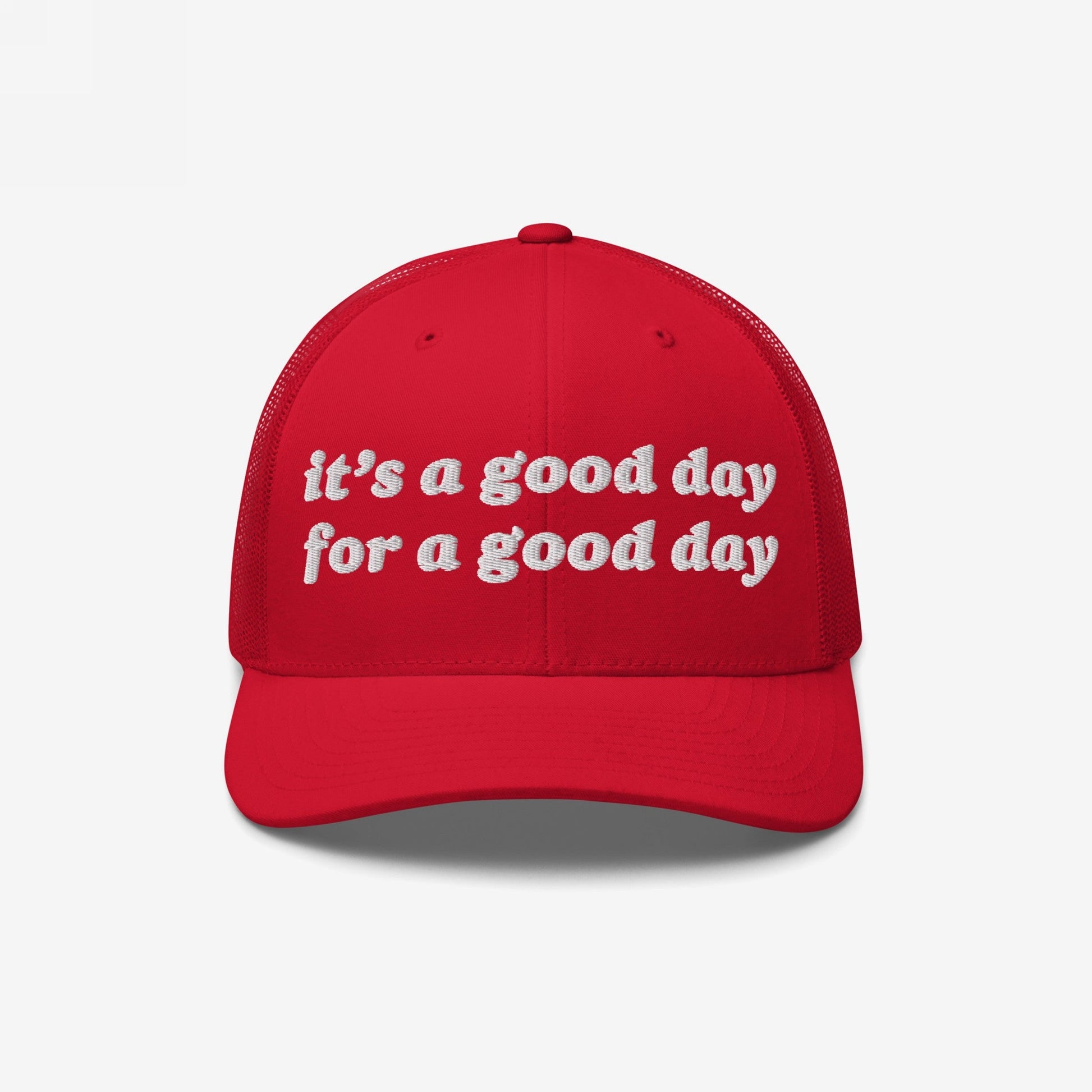 Red trucker-style baseball cap with white embroidered text reading “it’s a good day for a good day.” The Good Day Hat promotes positivity, featuring a curved bill and mesh back, supporting mental health awareness.