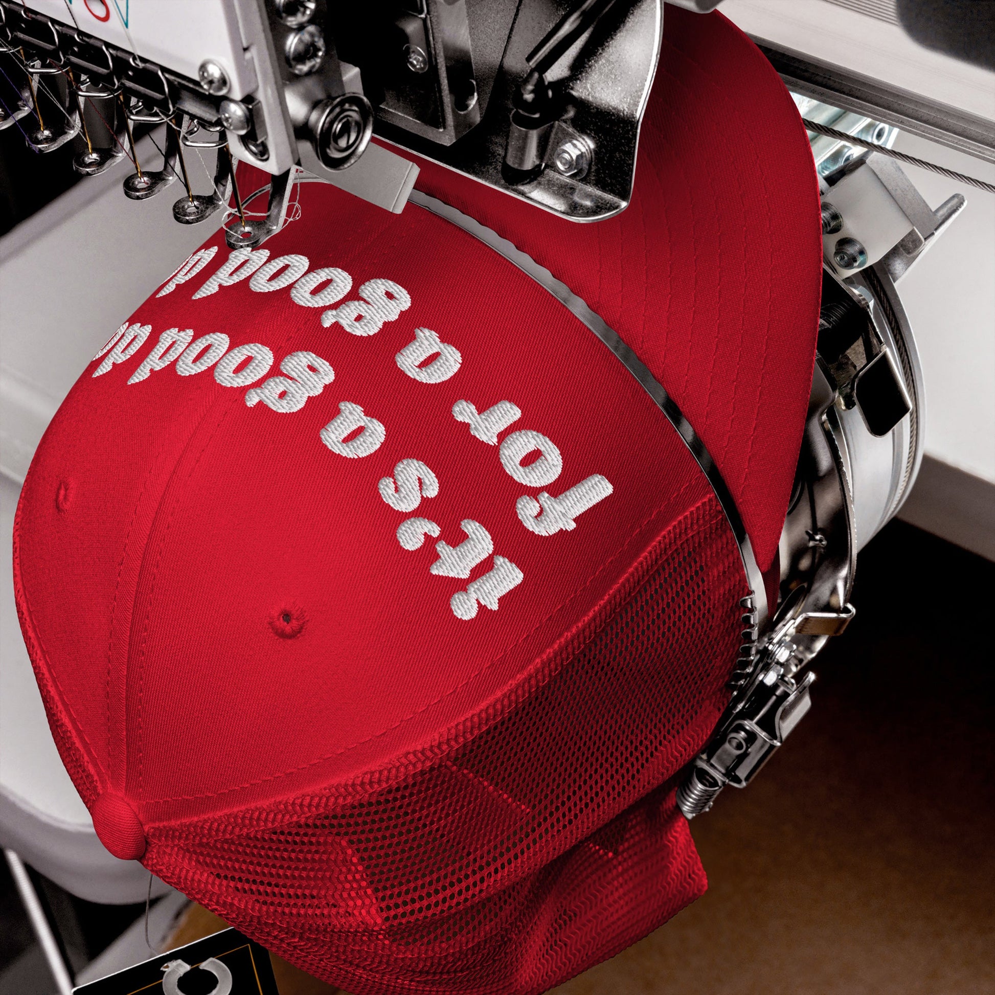 Good Day Hat clamped in an embroidery machine, white thread stitching It’s a good day for a good day on the front. Ideal for positivity advocates, available in various styles.