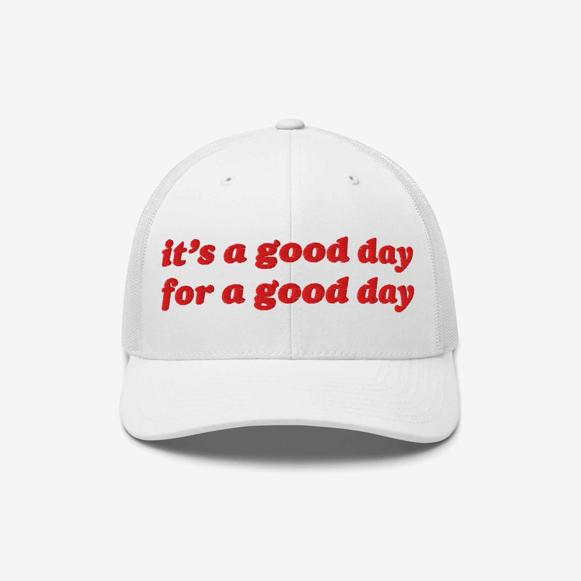 The Good Day Hat features a white trucker-style cap with a mesh back and curved brim, showcasing bright red embroidery reading it's a good day for a good day.