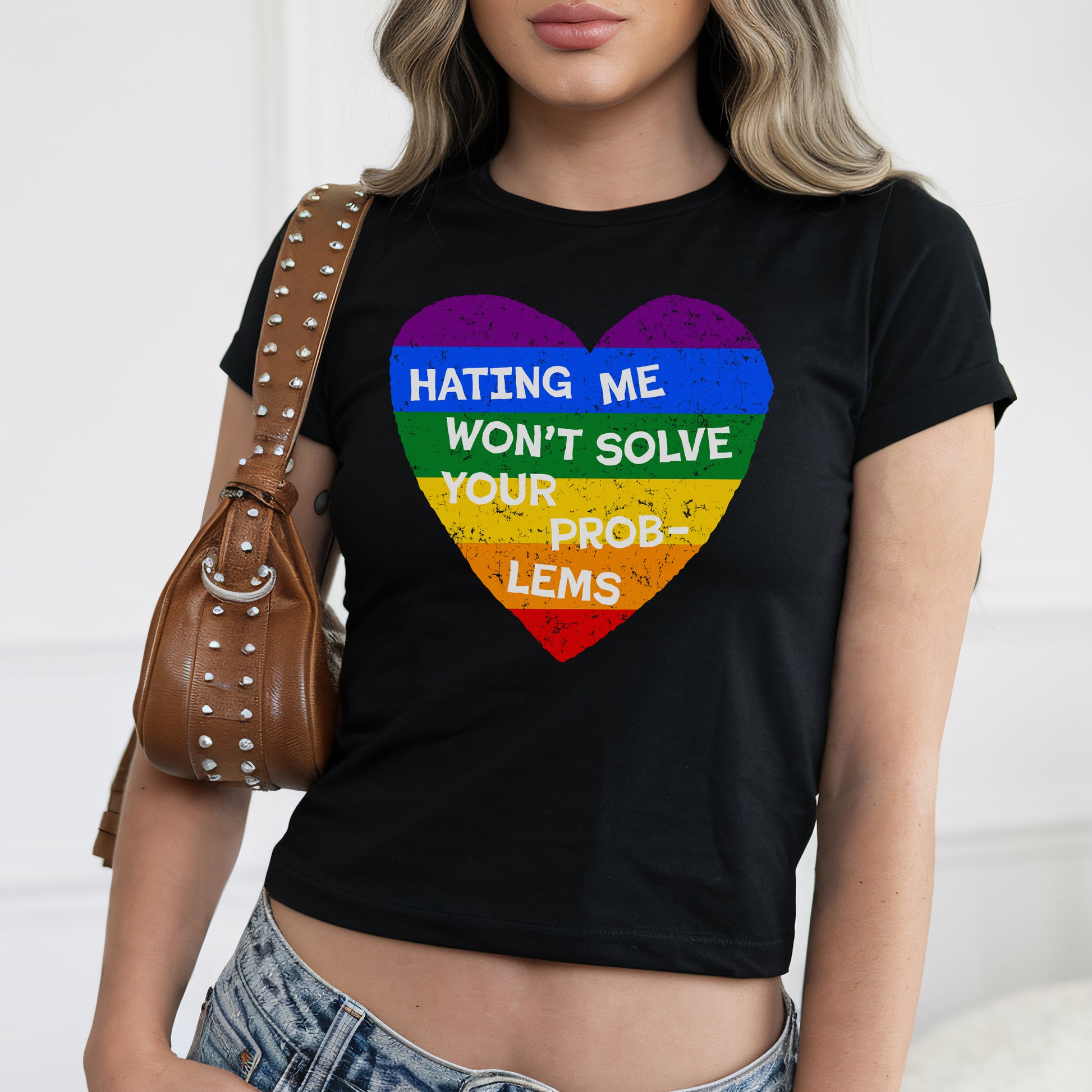 Woman wearing No LGBTQ Hate Women's Baby Tee black crop top with rainbow heart and slogan Hating Me Won't Solve Your Problems.