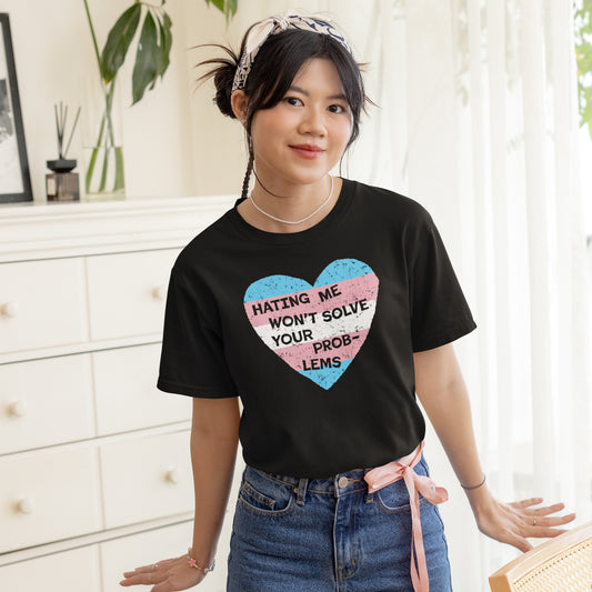 Young woman wearing the No Trans Hate Kids T-shirt EU, featuring a trans pride heart and empowering slogan, “HATING ME WON’T SOLVE YOUR PROBLEMS,” paired with high-waisted jeans, smiling indoors.