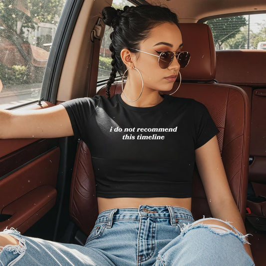 Woman wearing Timeline Women's Baby Tee black cropped shirt with white text sitting in car seat wearing sunglasses and hoop earrings