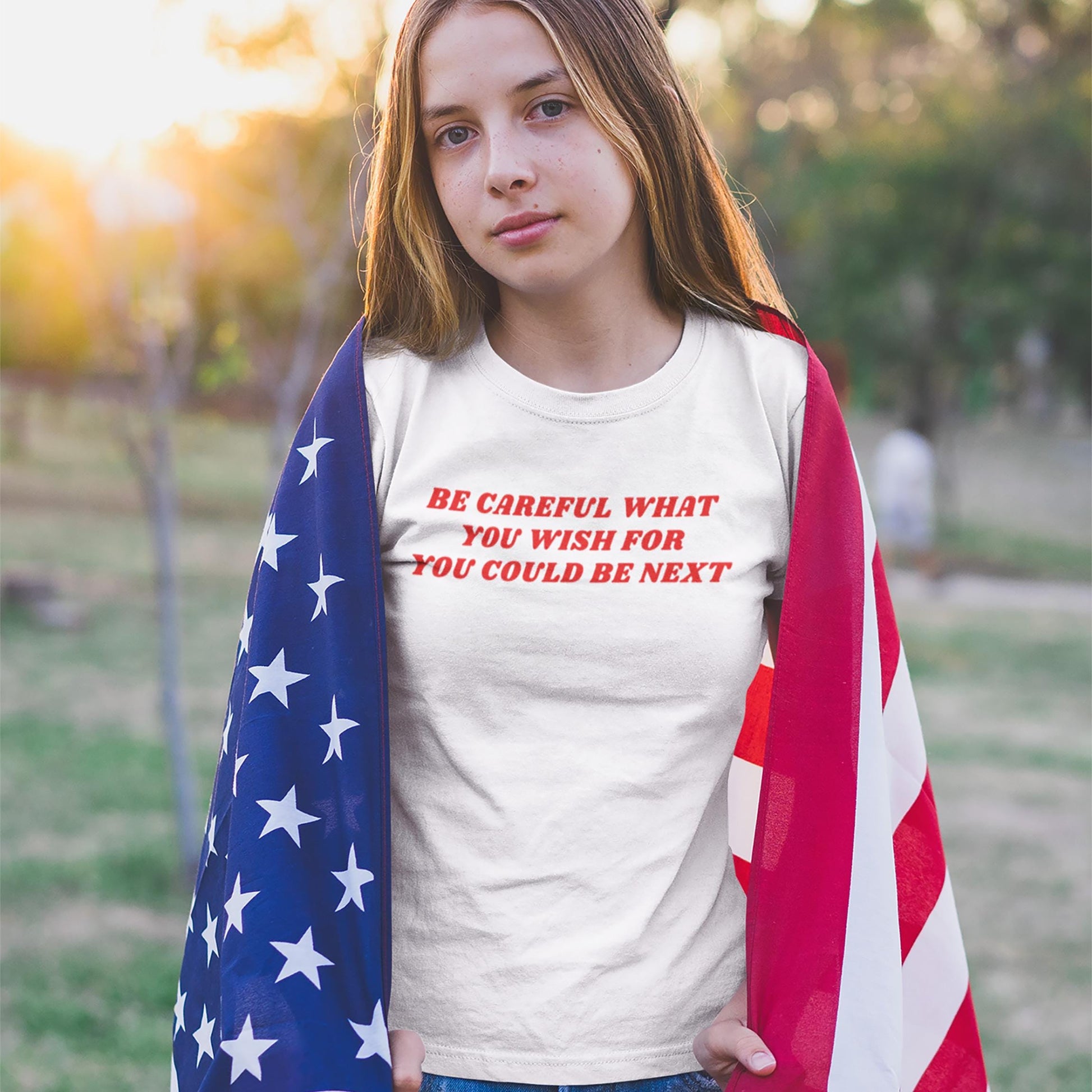 Young person outdoors wearing the Be Careful Kids T-shirt EU, featuring a bold slogan reminding viewers of vigilance. The shirt is designed for outspoken youth advocating for change and justice.