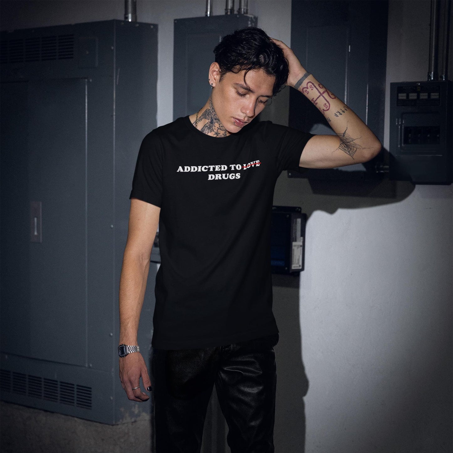 Model wearing a black "Addicted To Love / Drugs T-shirt" with bold white and red text in an industrial setting.