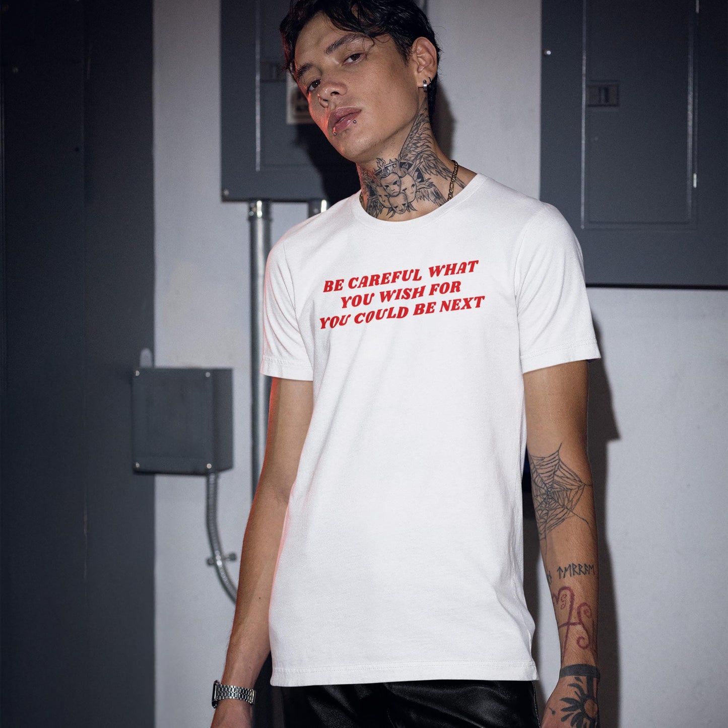 Young man wearing white Be Careful T-shirt with red text warning in urban setting, showcasing bold minimalism style.