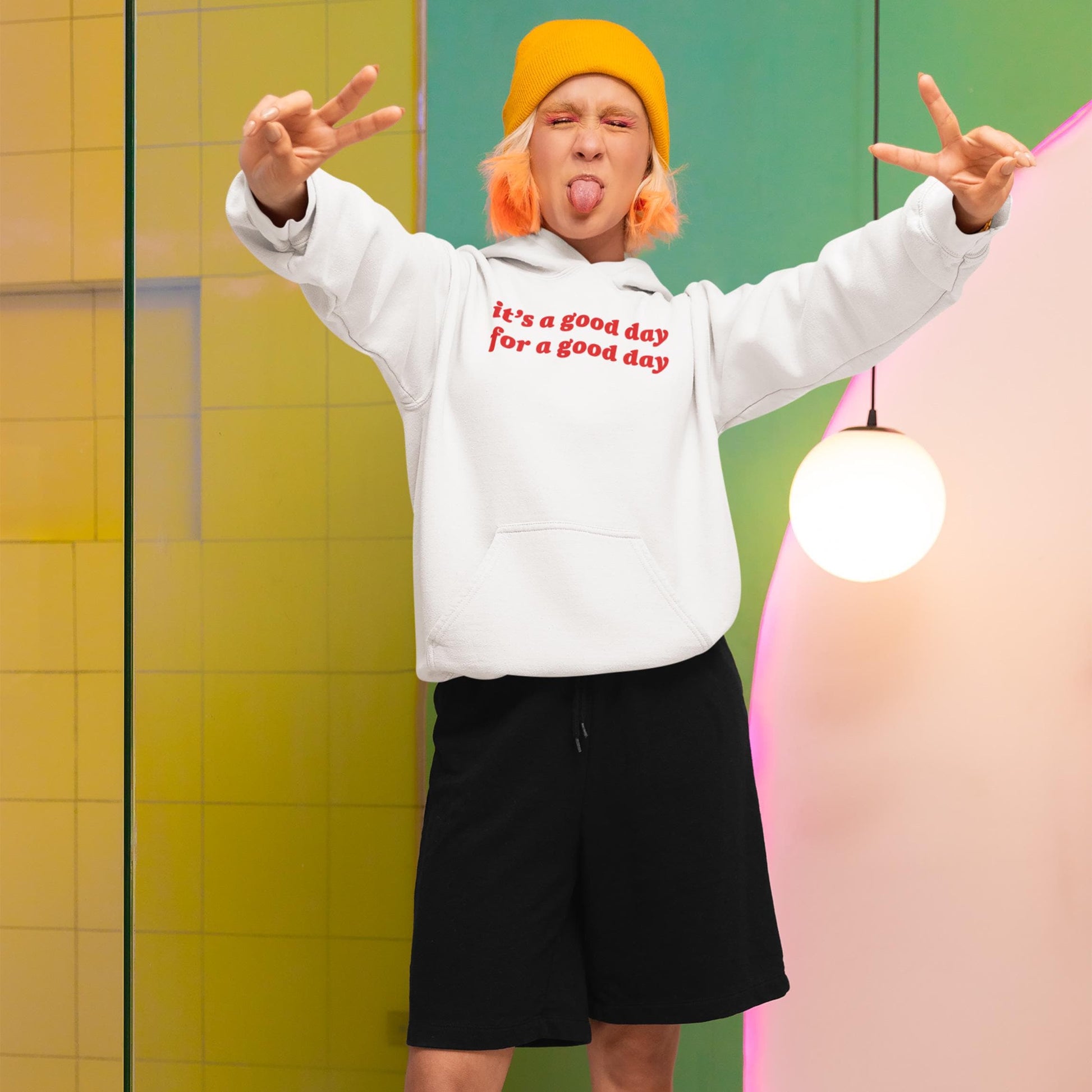 A young person playfully poses indoors wearing the Good Day Hoodie, featuring the uplifting slogan it's a good day for a good day, showcasing its cozy, mood-lifting design.