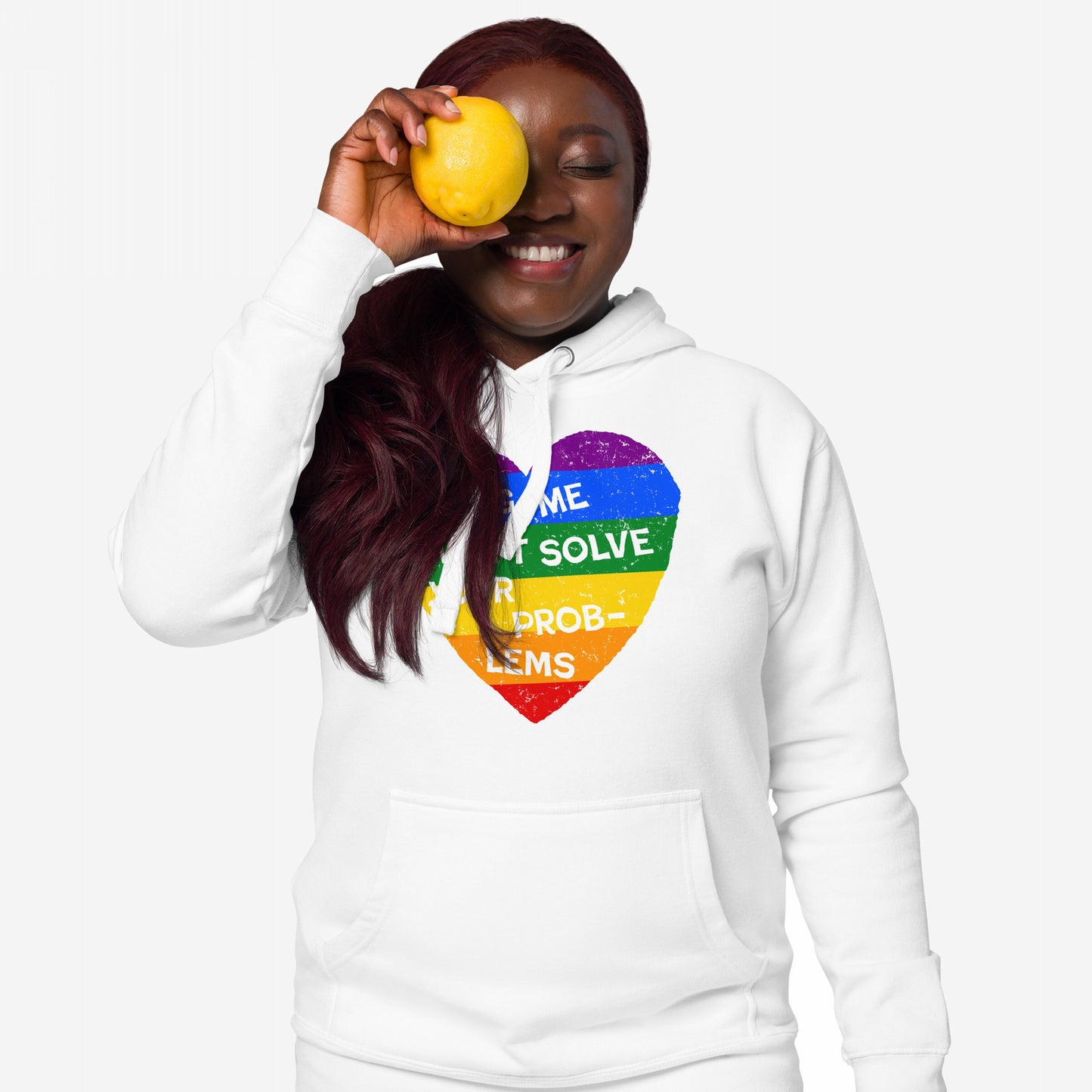 A dark-skinned person wears the No LGBTQ Hate Hoodie EU, showcasing a distressed rainbow heart with “Hating Me Won’t Solve Your Problems,” while playfully holding a lemon to their eye.