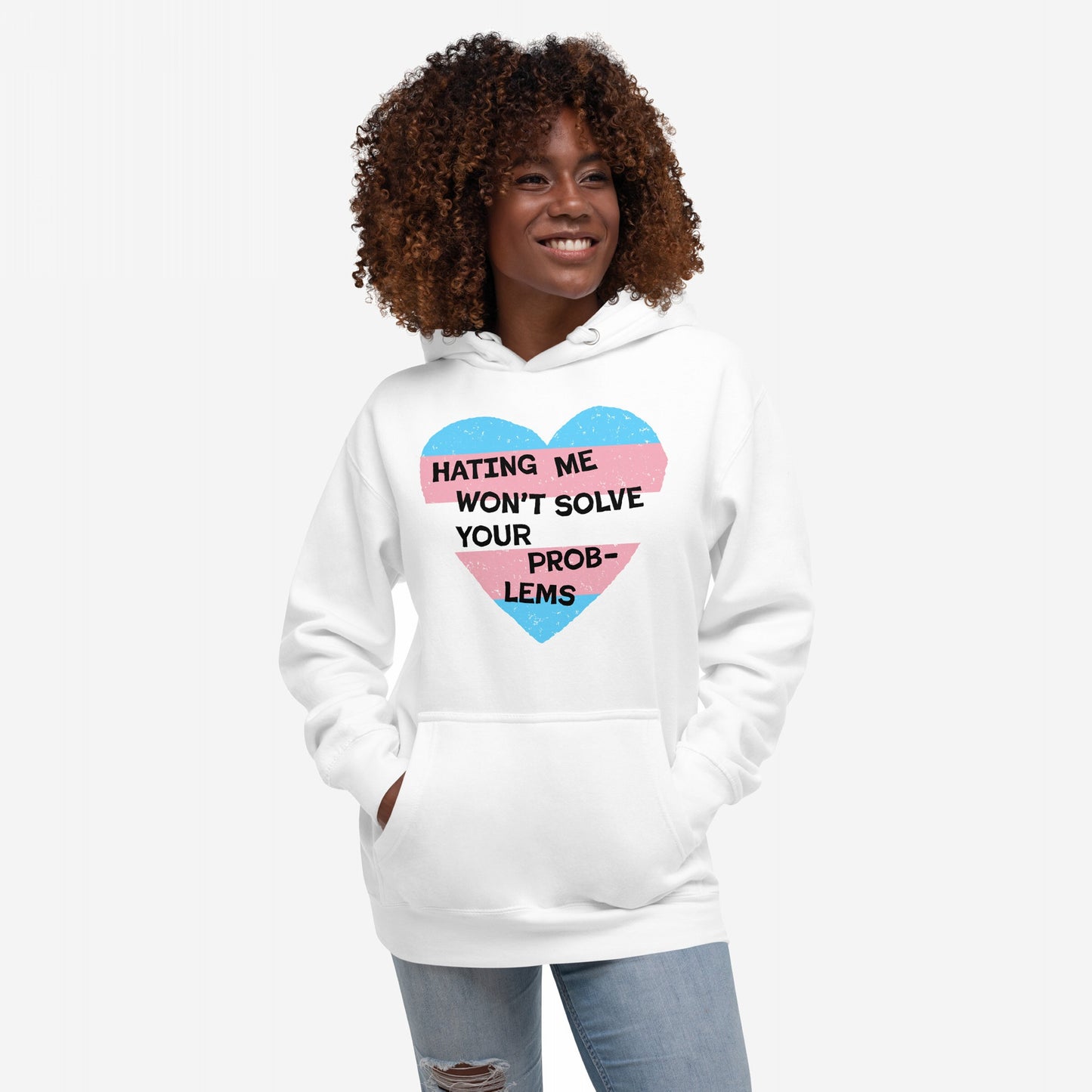 Person wearing the No Trans Hate Hoodie EU, featuring a heart with pastel stripes and the slogan “Hating Me Won’t Solve Your Problems,” hands in kangaroo pocket, against a plain background.