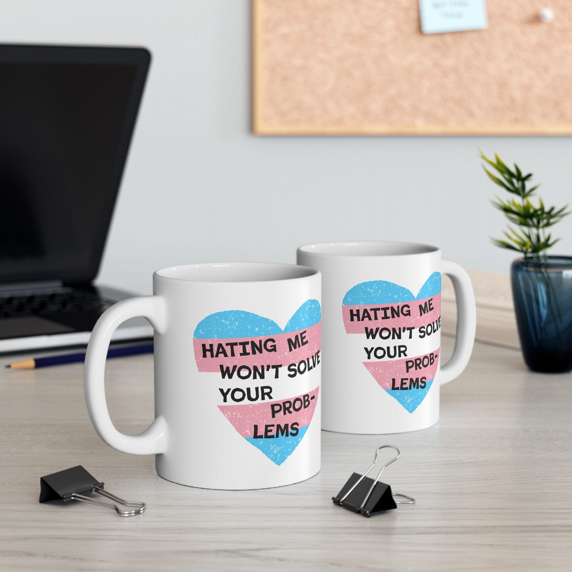 No Trans Hate Mug featuring a pastel-striped heart with the quote Hating Me Won’t Solve Your Problems, displayed on a white ceramic mug, emphasizing strength and gender identity.