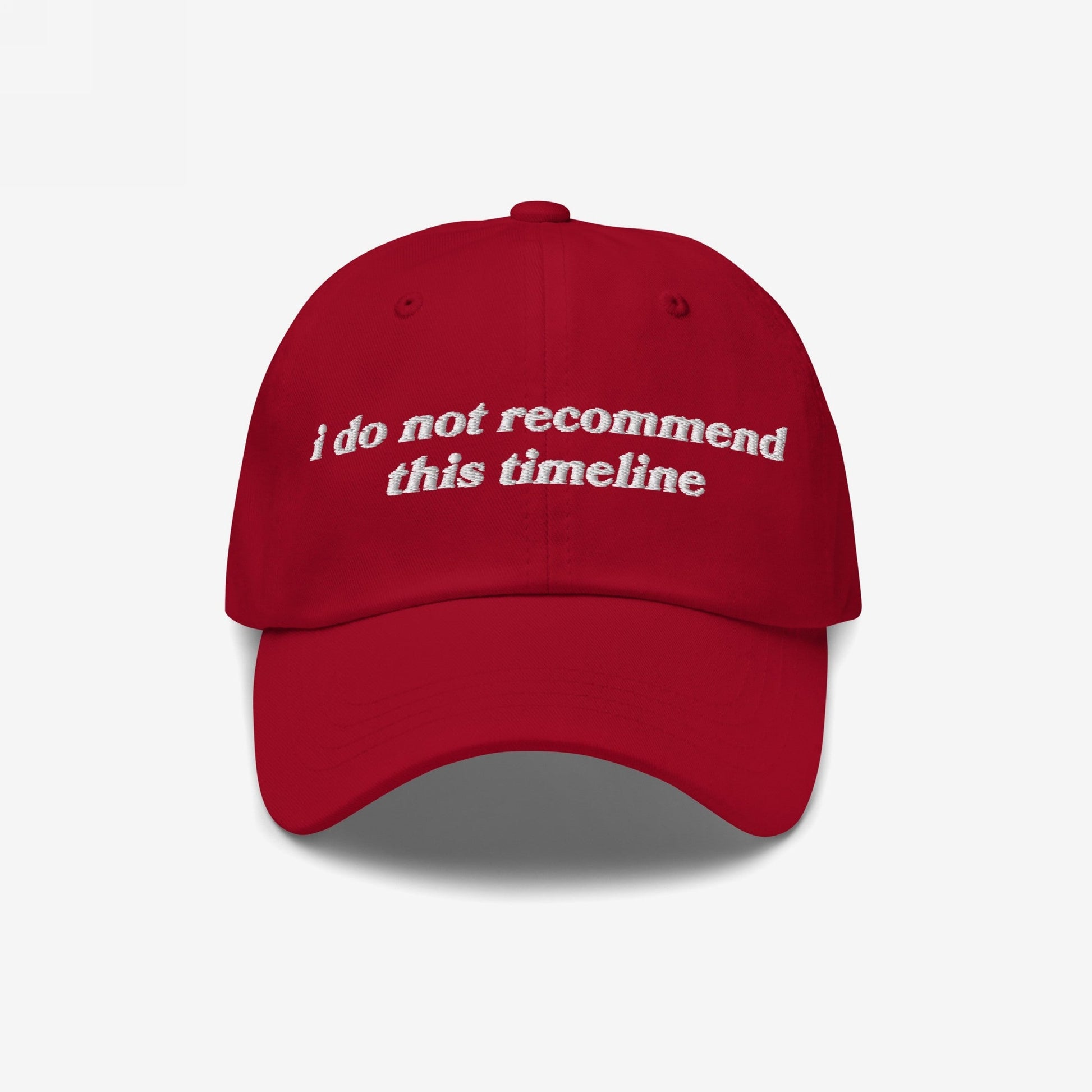 Red baseball-style cap with curved brim features I Do Not Recommend This Timeline in white embroidery, embodying Egoproof's blend of retro flair and modern, sarcastic commentary on current events.