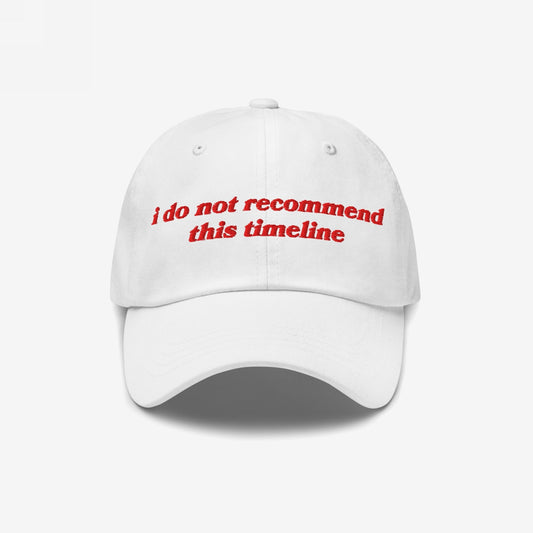 White cap with red embroidery reading i do not recommend this timeline, blending retro style with modern sarcasm. Ideal for expressing resilience and irony, supporting mental health awareness.