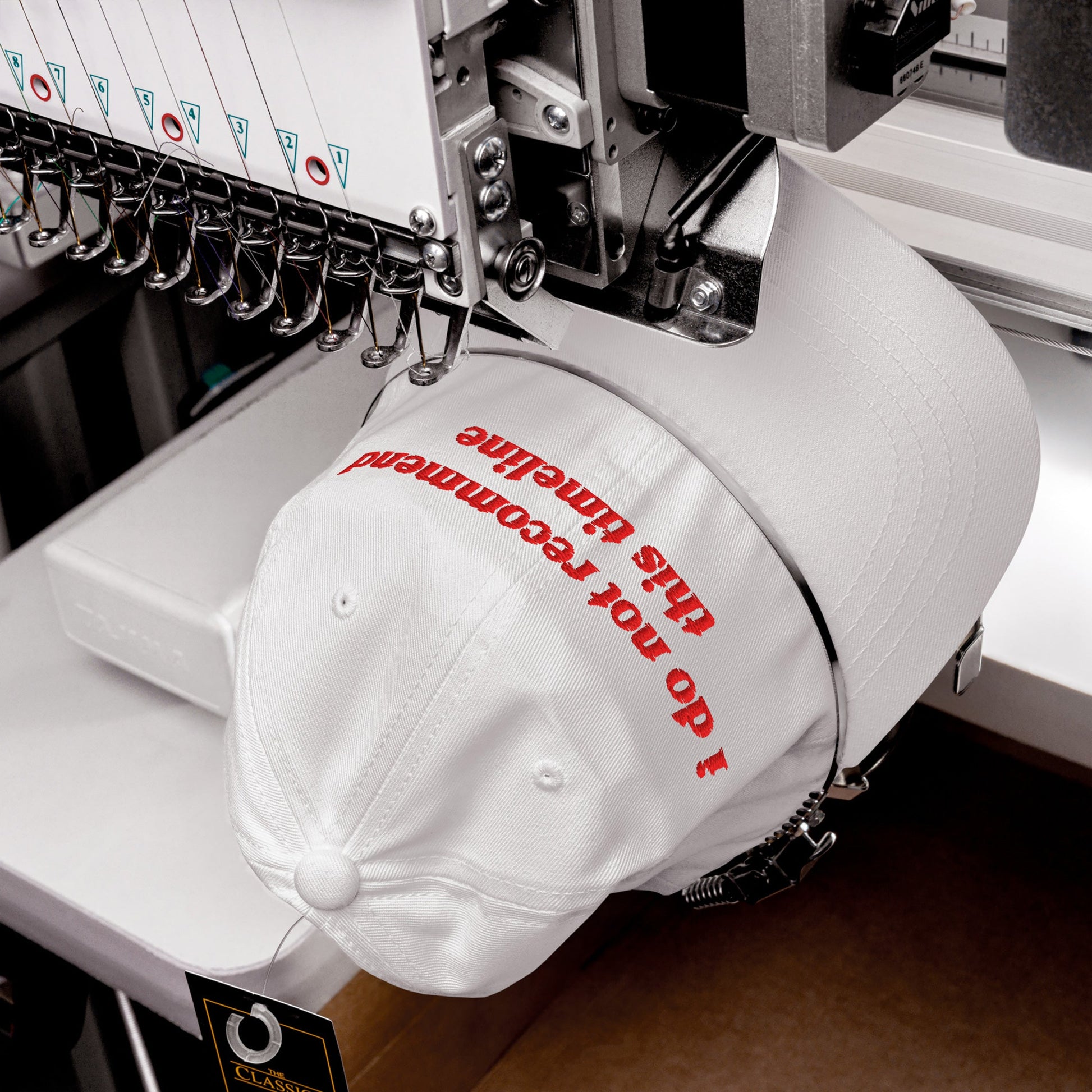 Timeline Hat with the phrase I do not recommend this timeline being embroidered by an industrial machine. The bold red thread and professional setup highlight its sarcastic statement and quality craftsmanship.