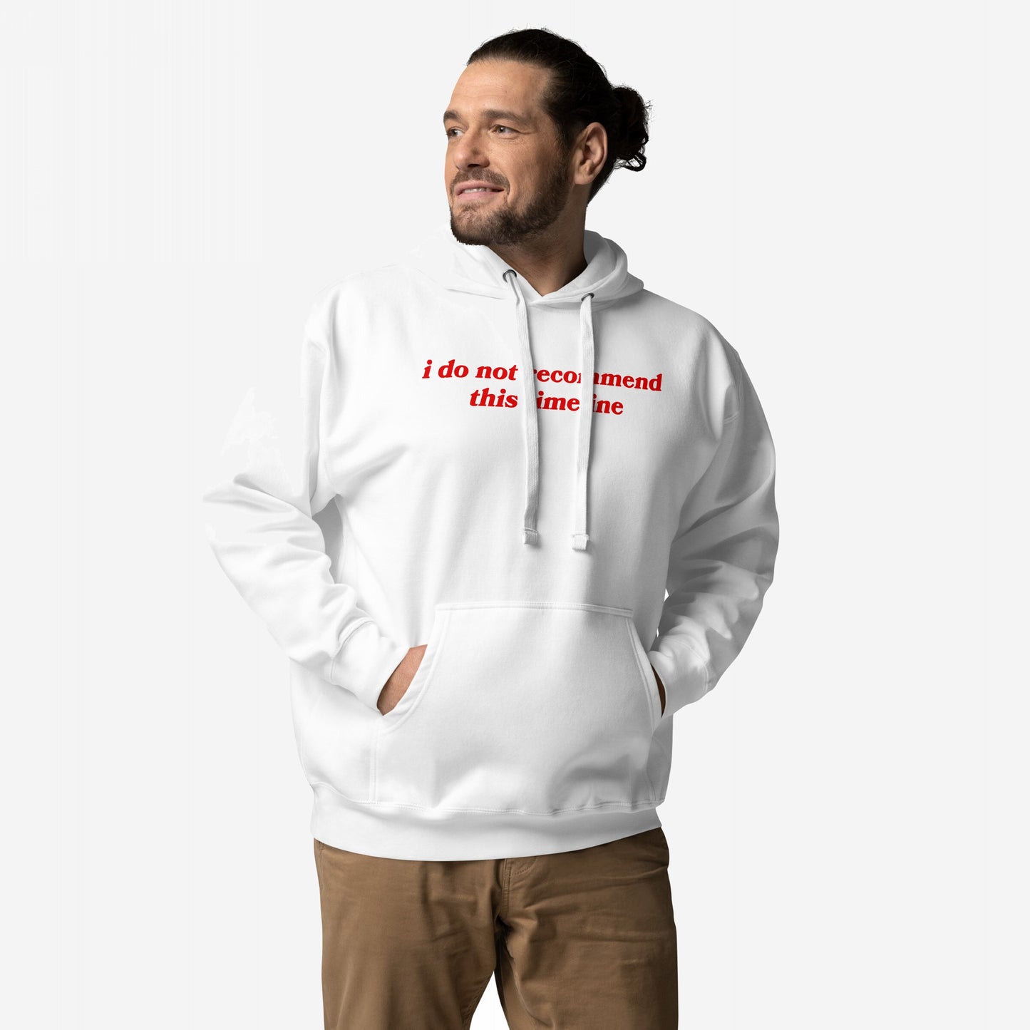 Man wearing the Timeline Hoodie EU, featuring i do not recommend this timeline in red across the chest, hands in kangaroo pocket, paired with brown pants against a simple backdrop.