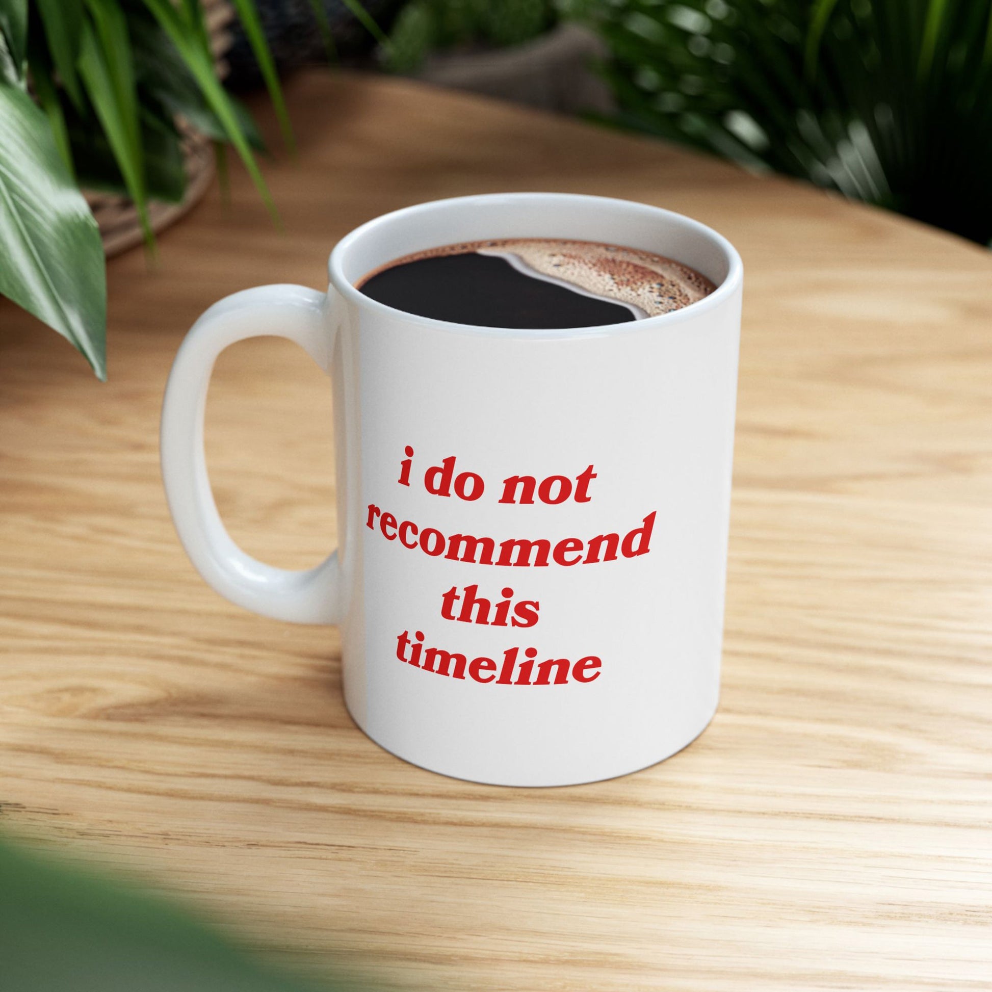 Timeline Mug: A white ceramic mug with the phrase “i do not recommend this timeline” in bold red letters, filled with coffee, on a wood table, embodying dry humor and resilience.