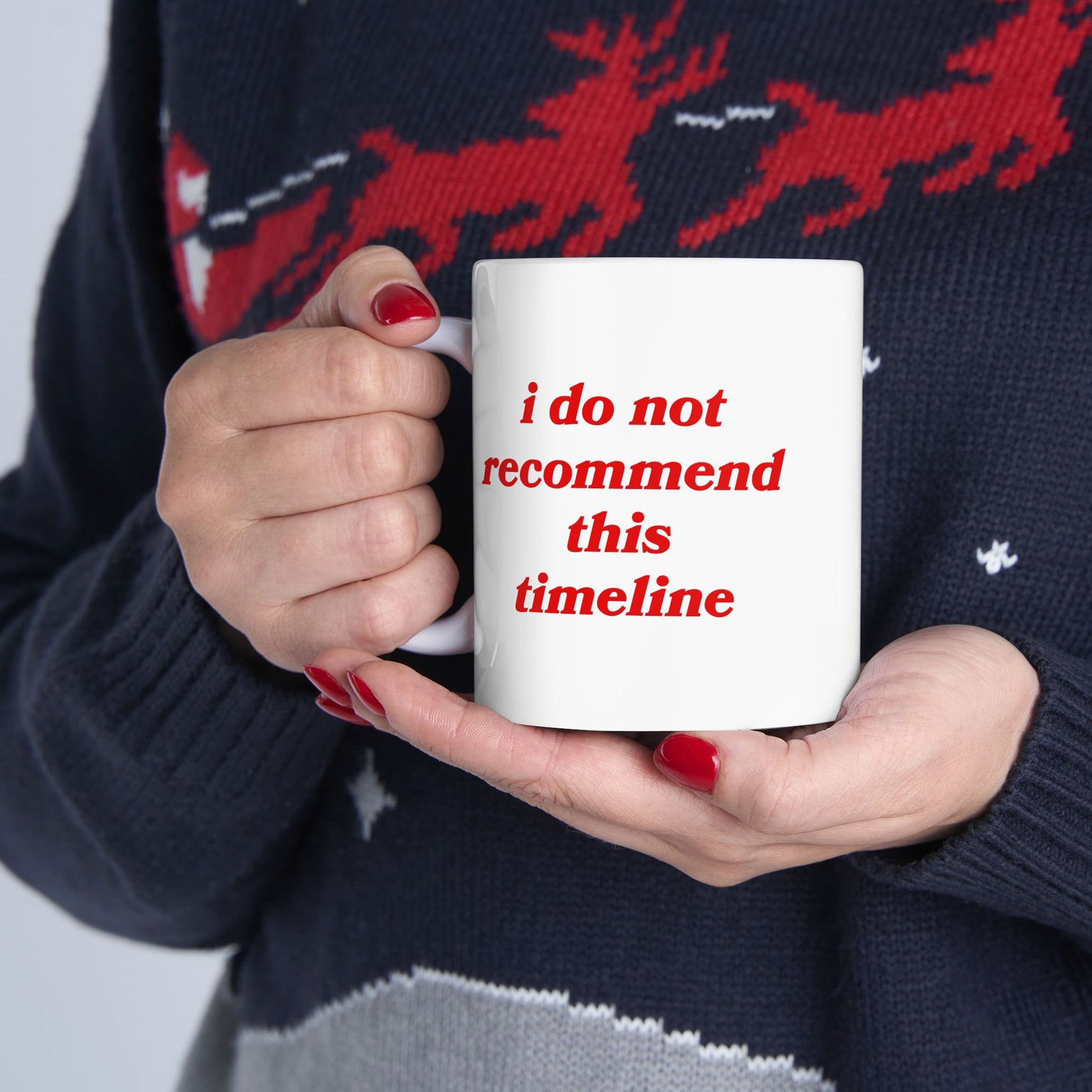 A person holds the Timeline Mug, featuring bold red text expressing dry humor. The mug, perfect for those navigating life's chaos, is ceramic, available in two sizes, and supports a mental health charity.