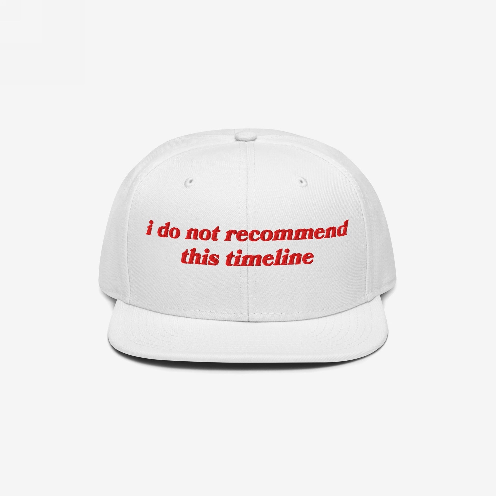 White flat-brim cap with red embroidered text, I Do Not Recommend This Timeline, capturing sarcasm and resilience. Ideal for expressing irony in chaotic times.