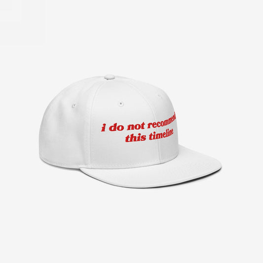White flat-brim snapback hat with red embroidered text reading i do not recommend this timeline. The Timeline Hat embodies sarcasm and resilience, ideal for those navigating modern chaos with humor.