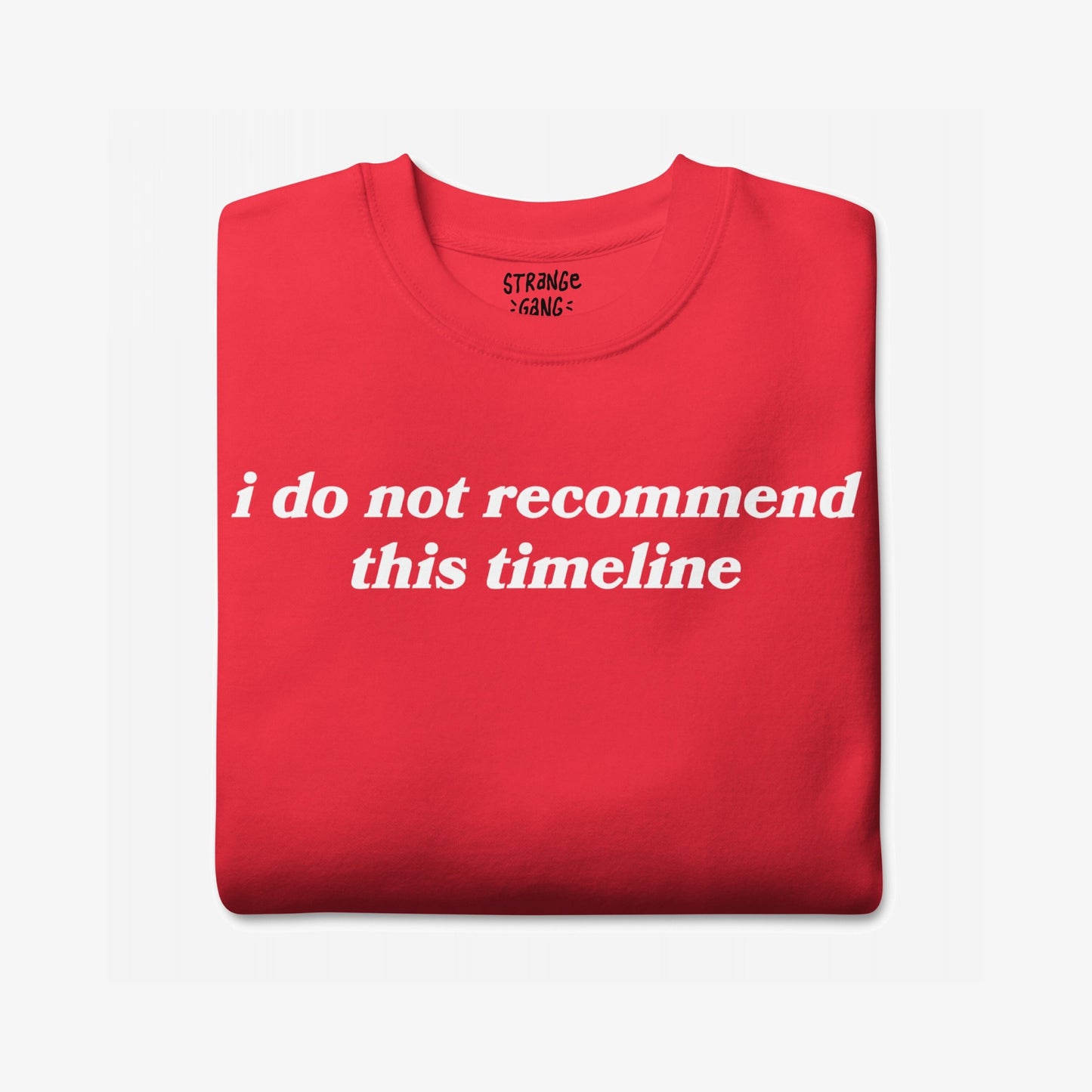 Folded red sweatshirt displaying bold white text: “i do not recommend this timeline.” Aimed at doomsday scrollers, the Timeline Sweatshirt EU offers a sarcastic take on modern life's absurdity.