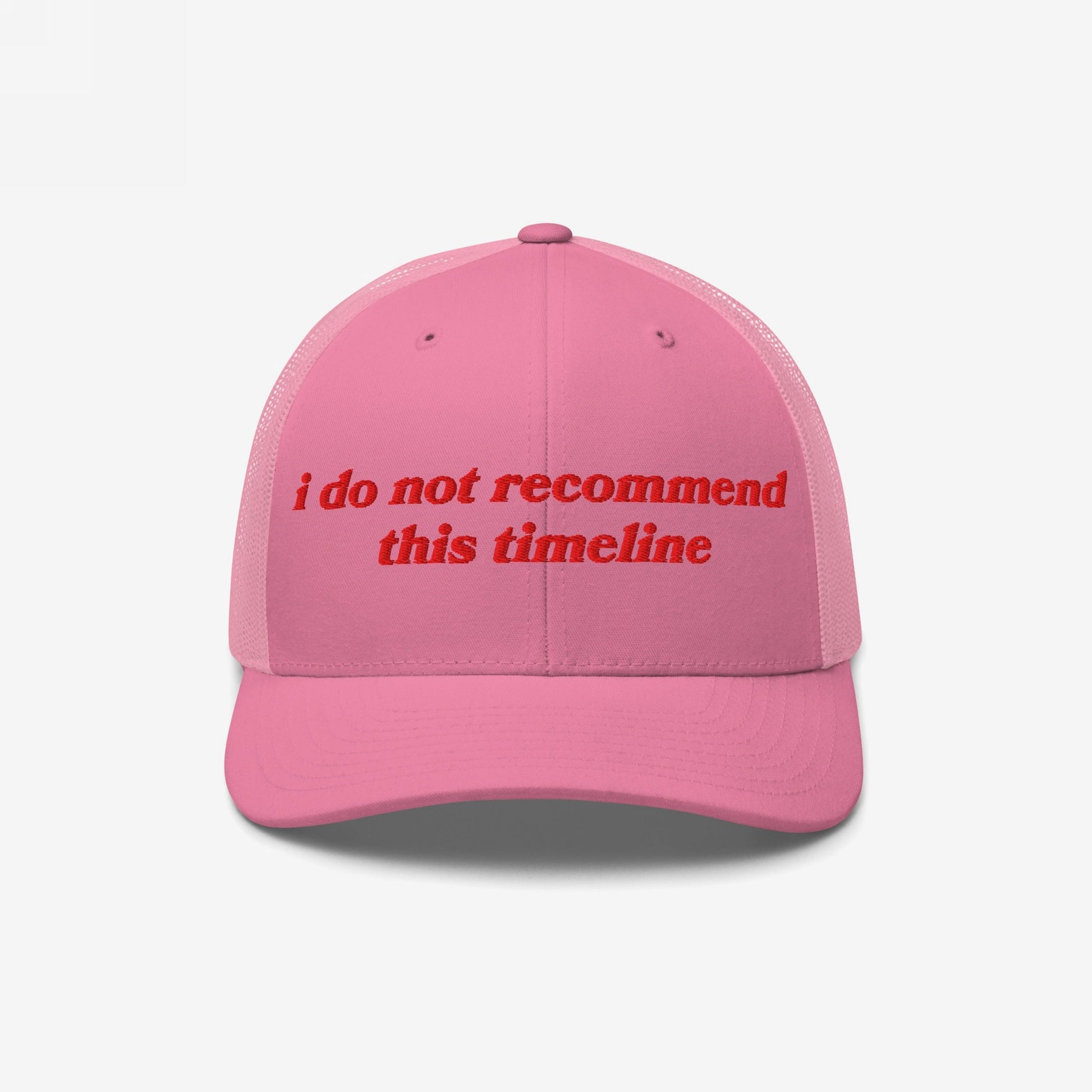 Pink mesh-back trucker cap with red embroidery reading “i do not recommend this timeline.” The Timeline Hat blends retro and modern, ideal for those embracing irony amidst chaos.
