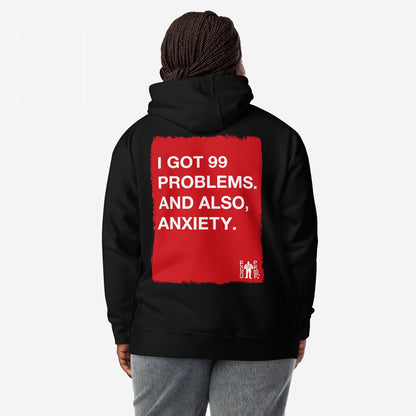 99 Problems Hoodie EU features a bold red square with white text about stress and anxiety on the back, worn by a person with braided hair in gray pants.